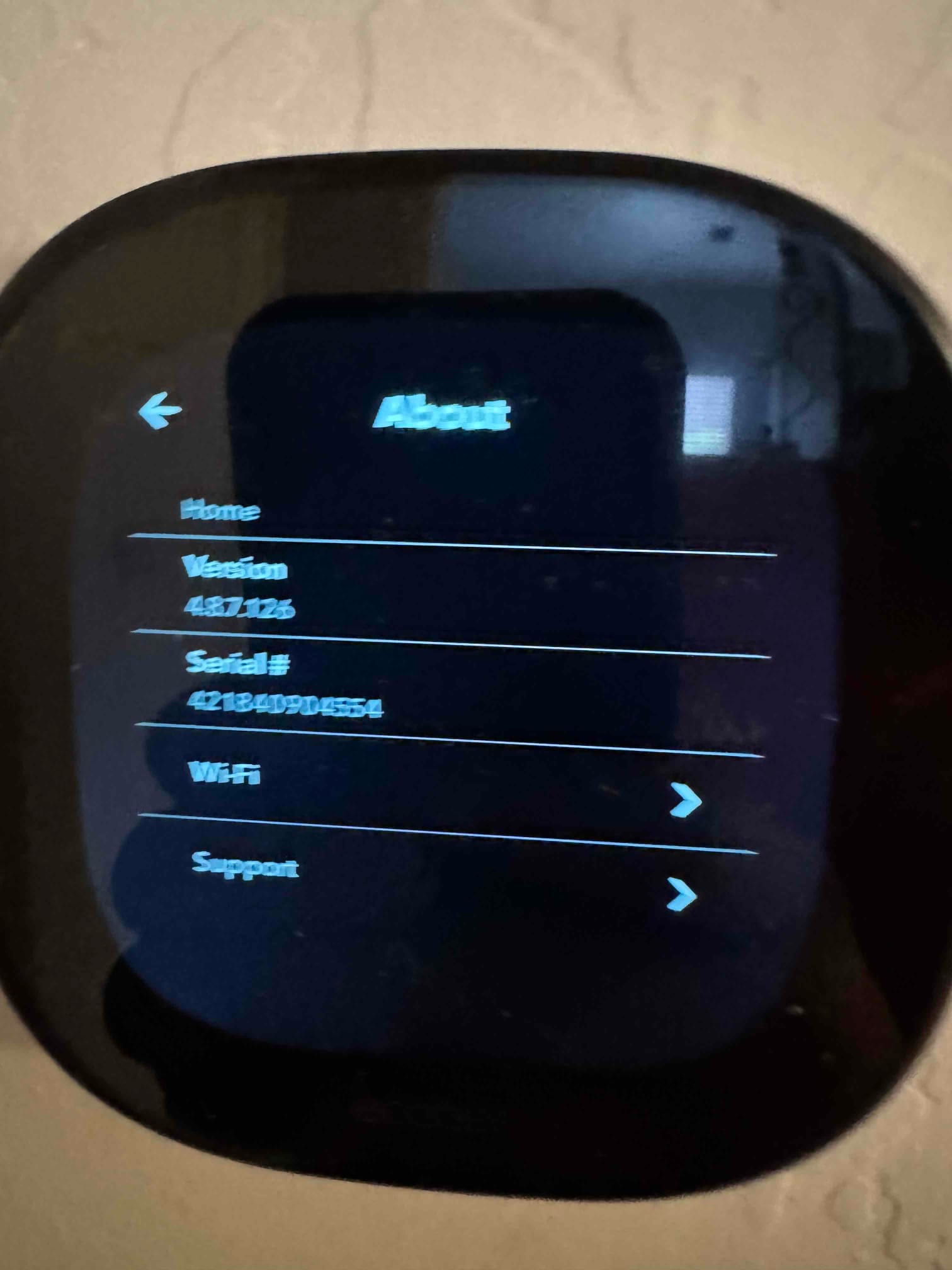 Wall-mounted smart thermostat shows an About screen with version and Wi‑Fi options during setup after installation.