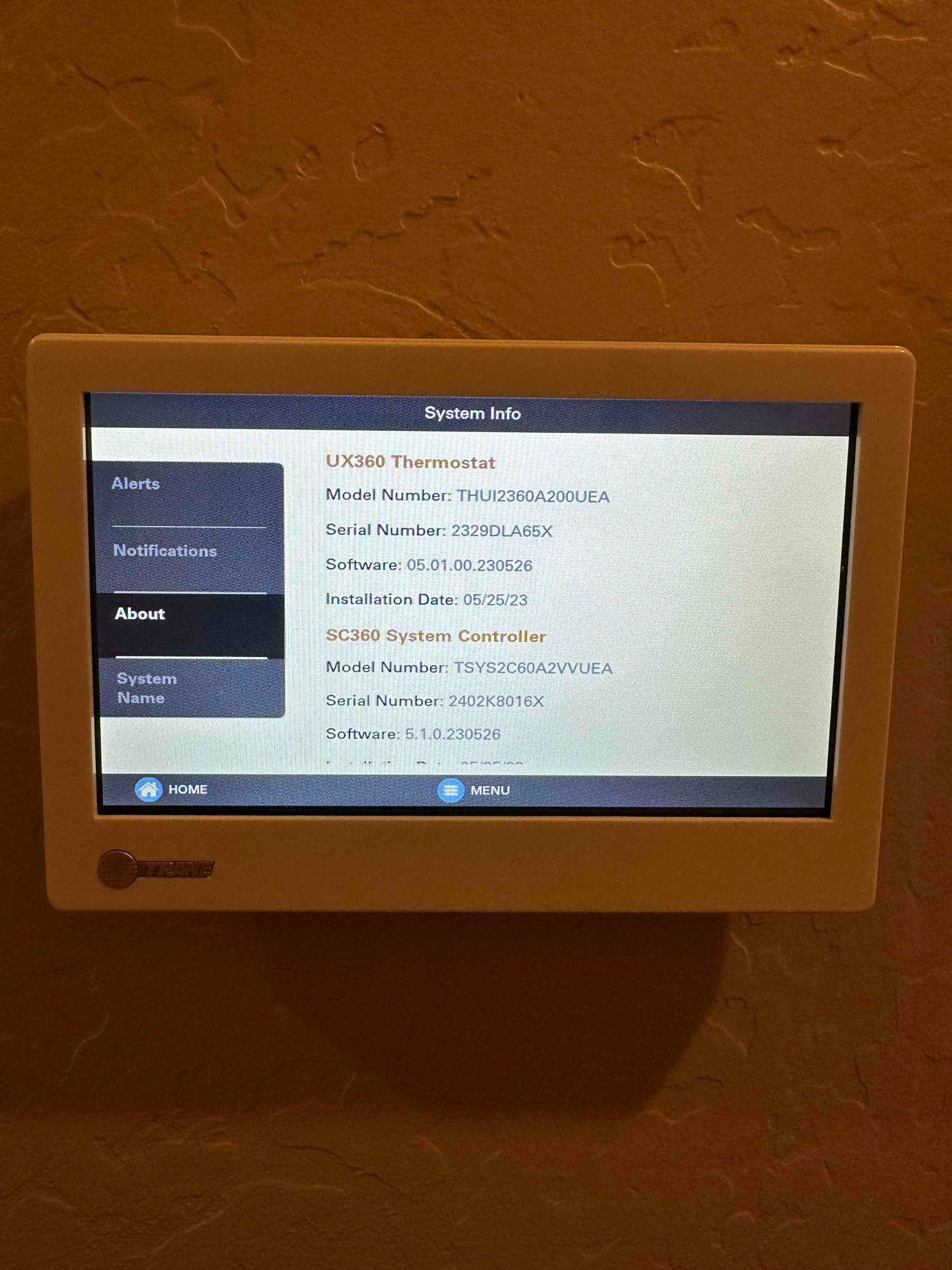 Wall-mounted thermostat touchscreen displays system information and software details after installation.