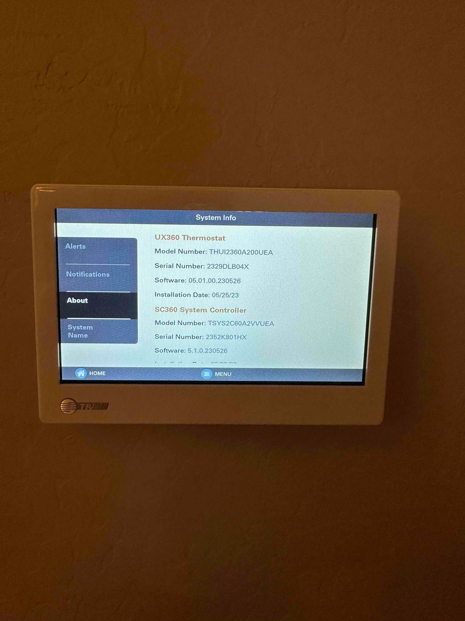 Wall-mounted touchscreen thermostat displays system information menu after installation.