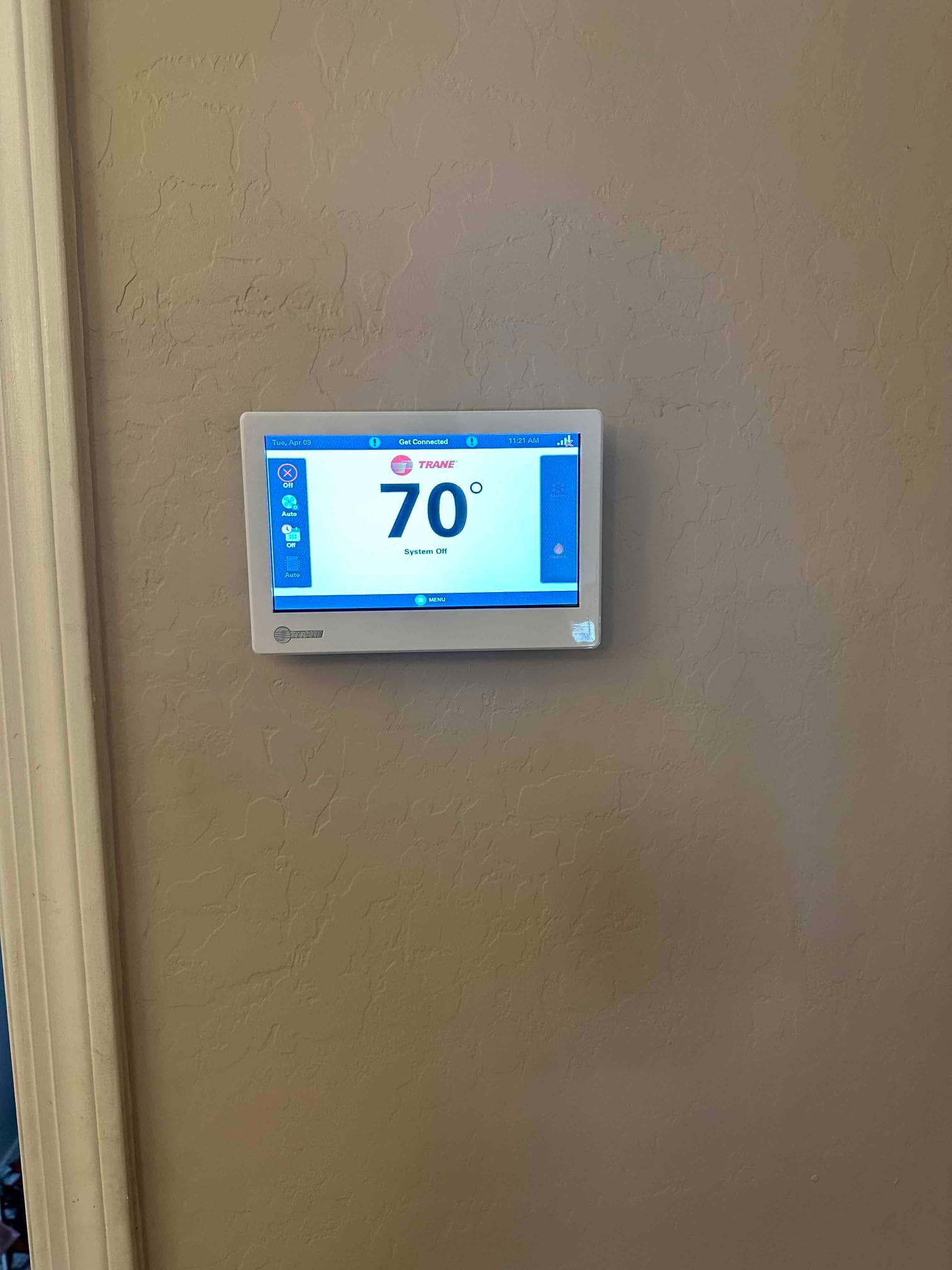 Wall-mounted touchscreen thermostat installed and powered on, displaying 70 degrees with the HVAC system currently off.