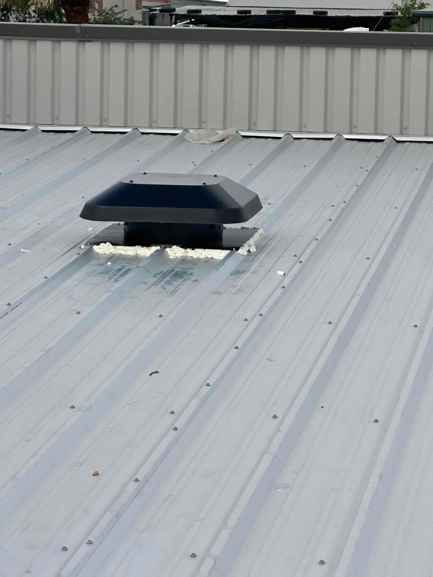 Low-profile roof vent installed on a metal roof, sealed around the base with foam for weather protection.