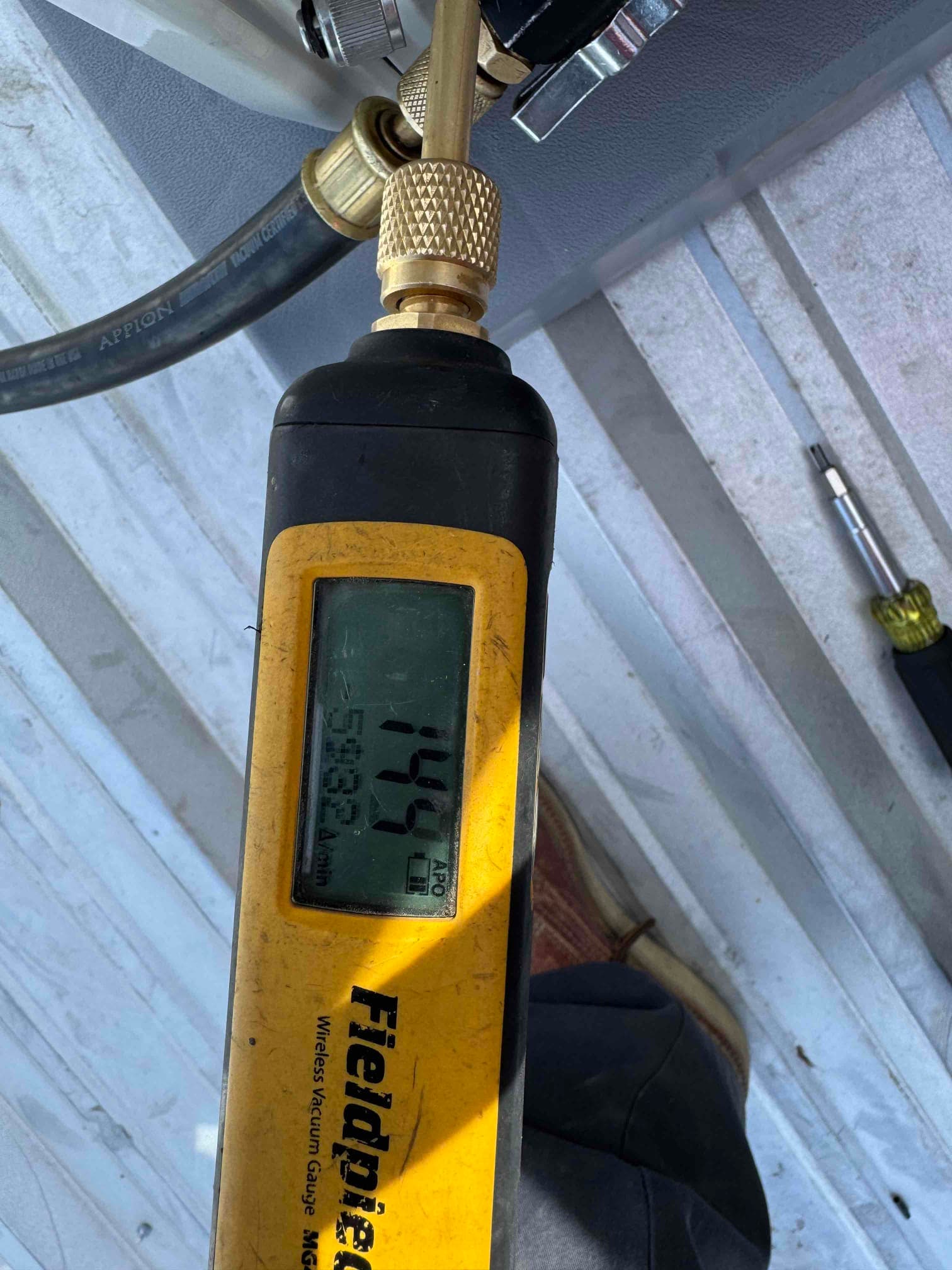 Micron gauge connected at the service port reads 144 microns, confirming a deep vacuum before releasing refrigerant charge.