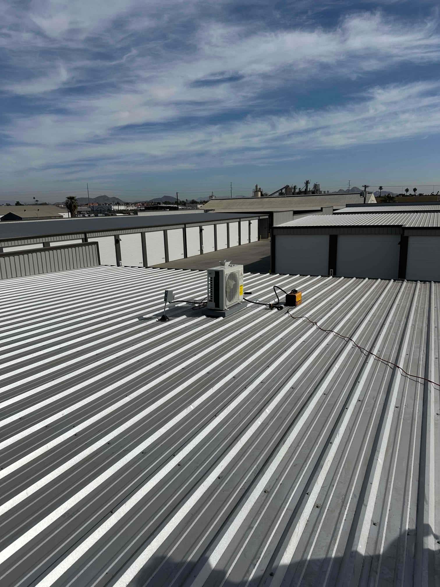 Mini‑split outdoor unit mounted on a metal rooftop with line set supports and electrical whip routed across the roof.