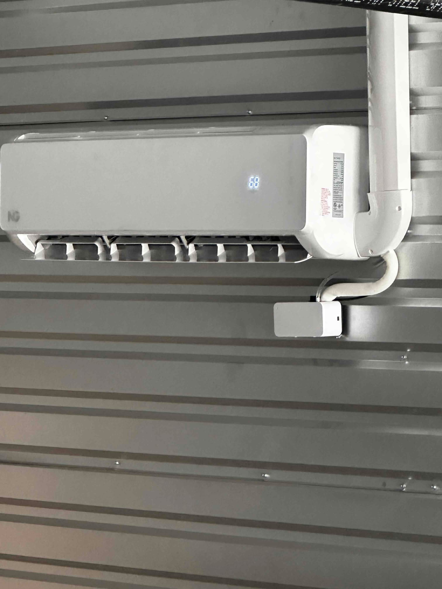 Wall-mounted mini-split indoor unit installed with line set cover and drain routing; display shows 68 on the front panel.