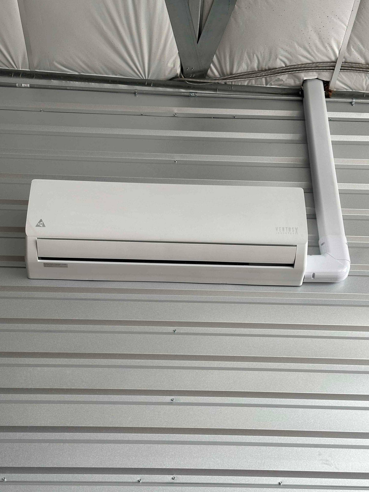Wall-mounted mini-split indoor unit installed on metal interior wall with line set concealed in a matching surface conduit.