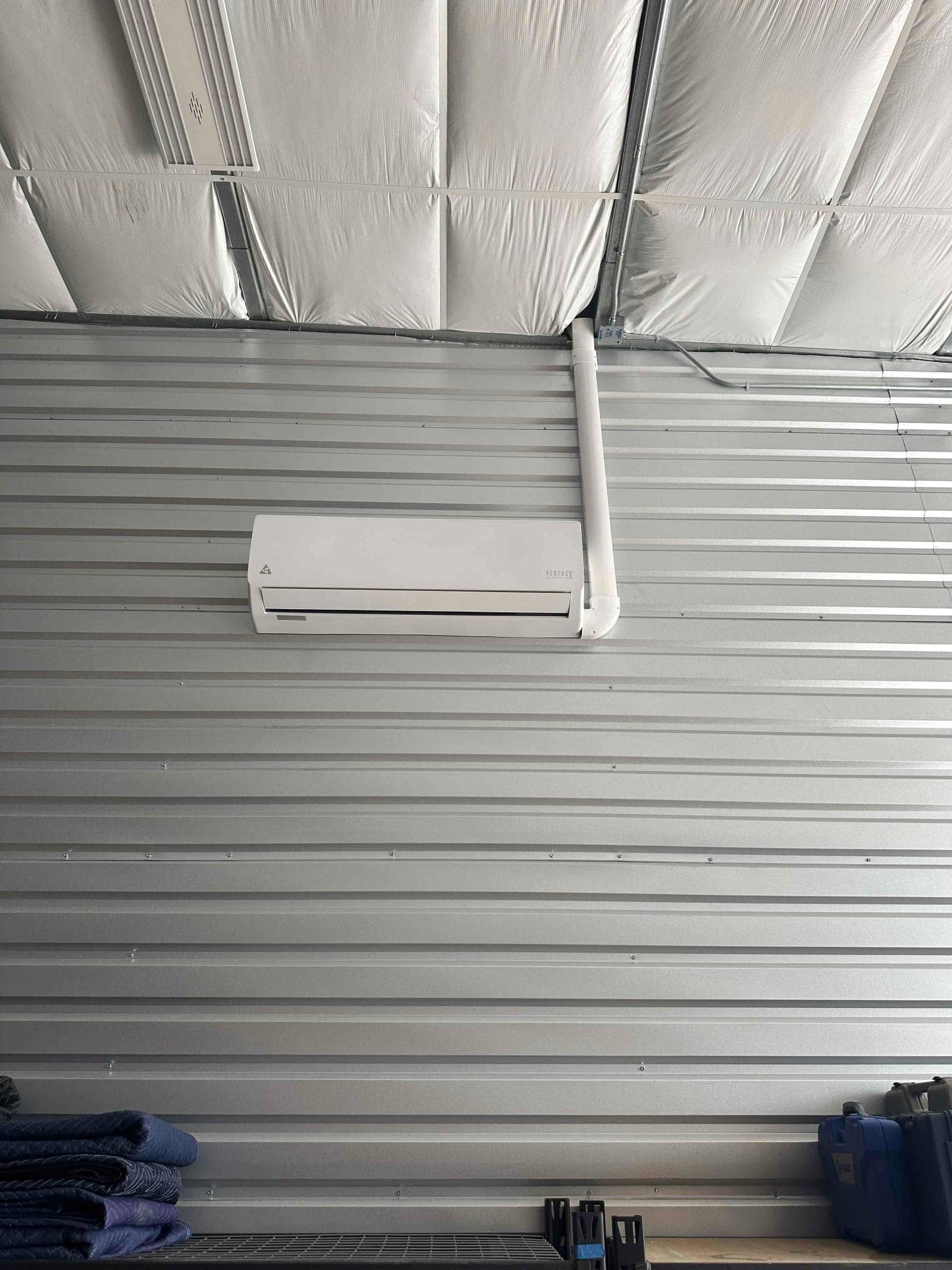 Wall-mounted mini-split indoor unit installed on metal wall with line-set cover routed upward toward the ceiling.