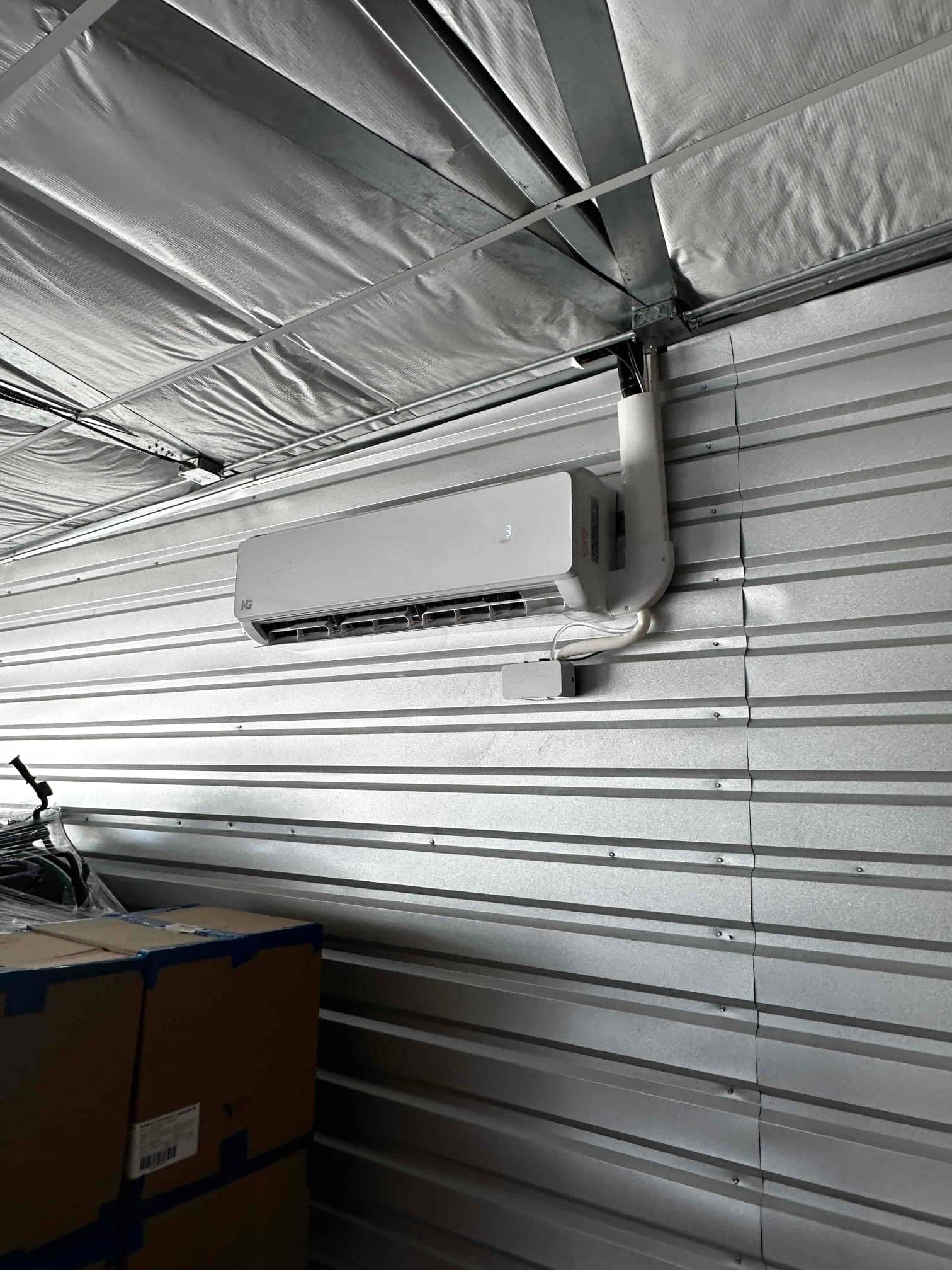 Wall-mounted mini-split indoor unit installed on a metal wall with line set cover and condensate drain routed upward.