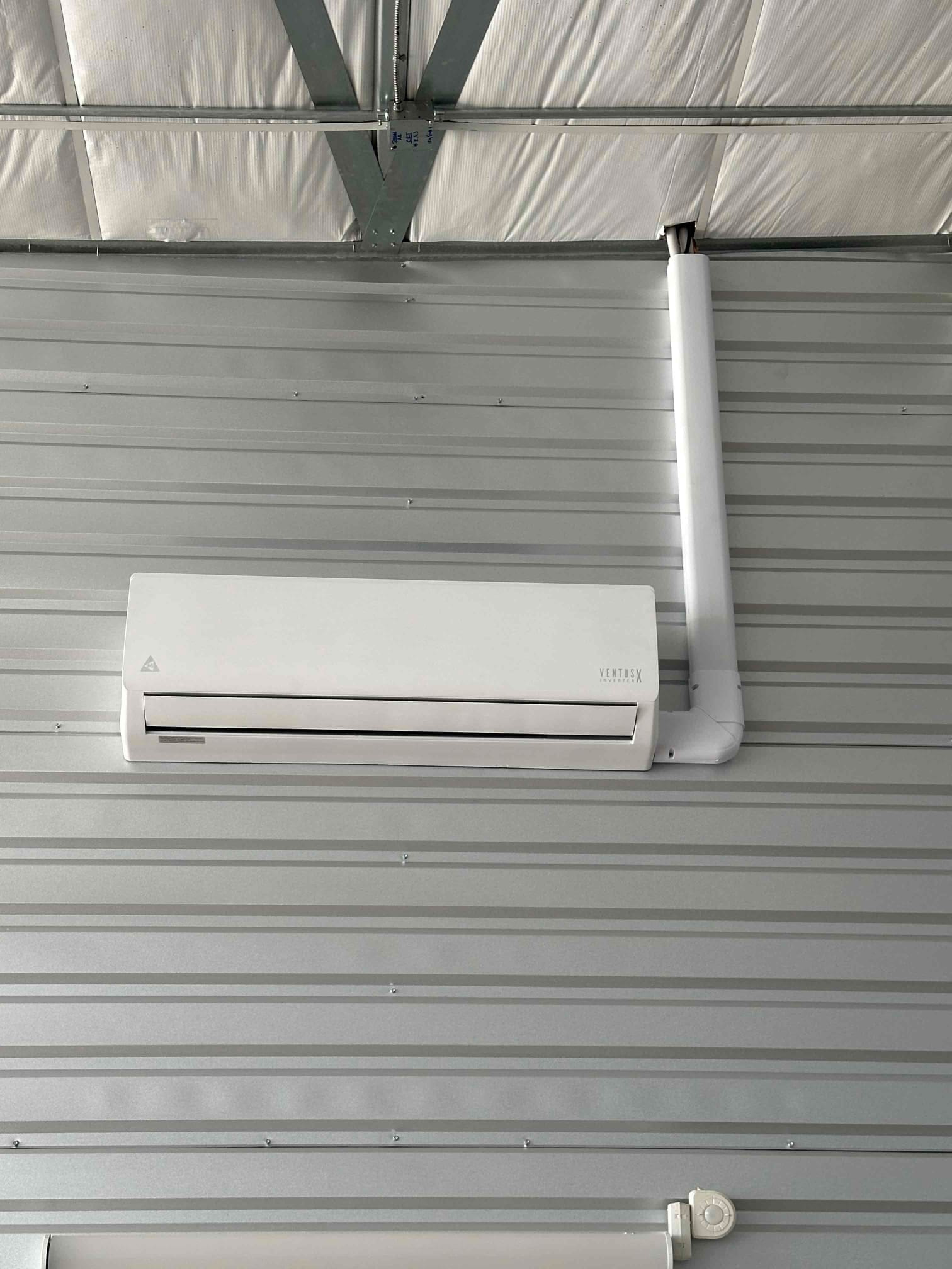 Wall-mounted mini-split indoor unit installed on metal paneling with neatly routed line-set cover extending to the ceiling.