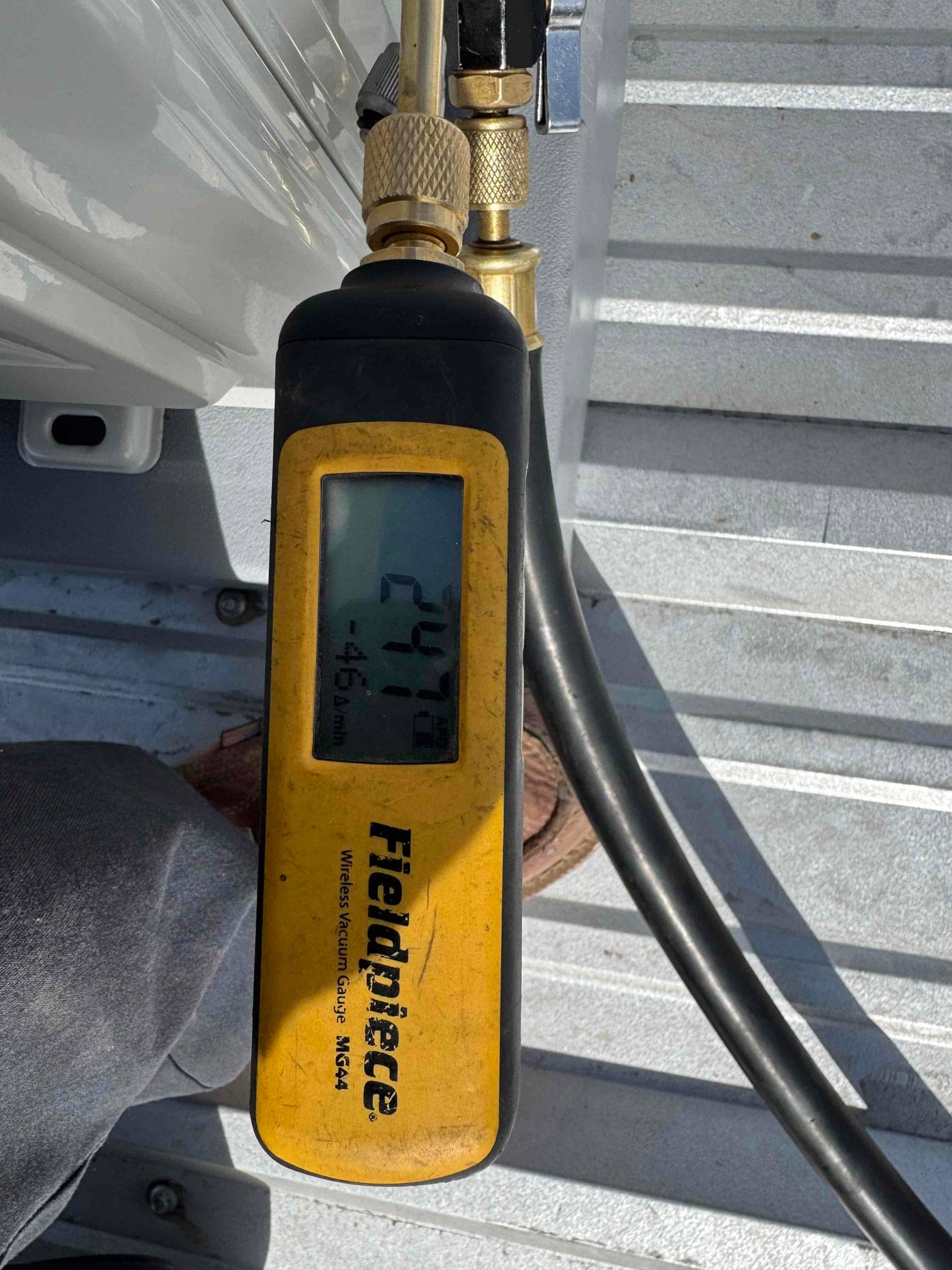 Wireless vacuum gauge connected to the system shows 247 microns, confirming deep evacuation before releasing refrigerant charge.