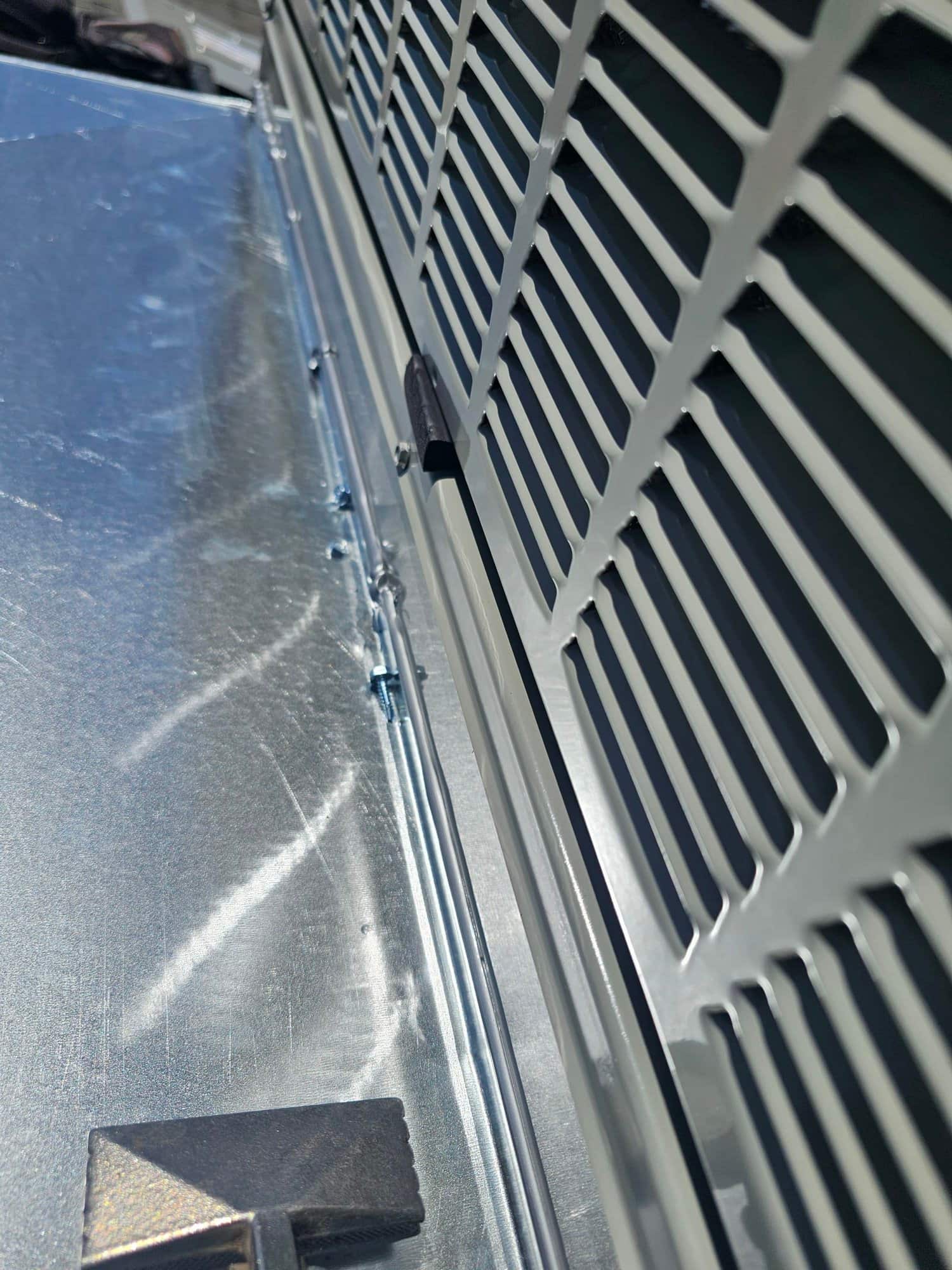 Close-up of new outdoor condenser housing aligned with a fabricated sheet metal curb or flashing, showing fasteners and clean installation seams.