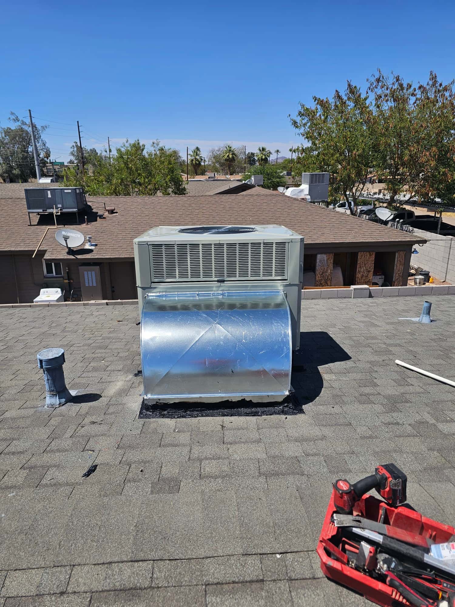 New rooftop package unit installed with sealed curb and sheet metal transition, photographed from the roof alongside tools used for the install.