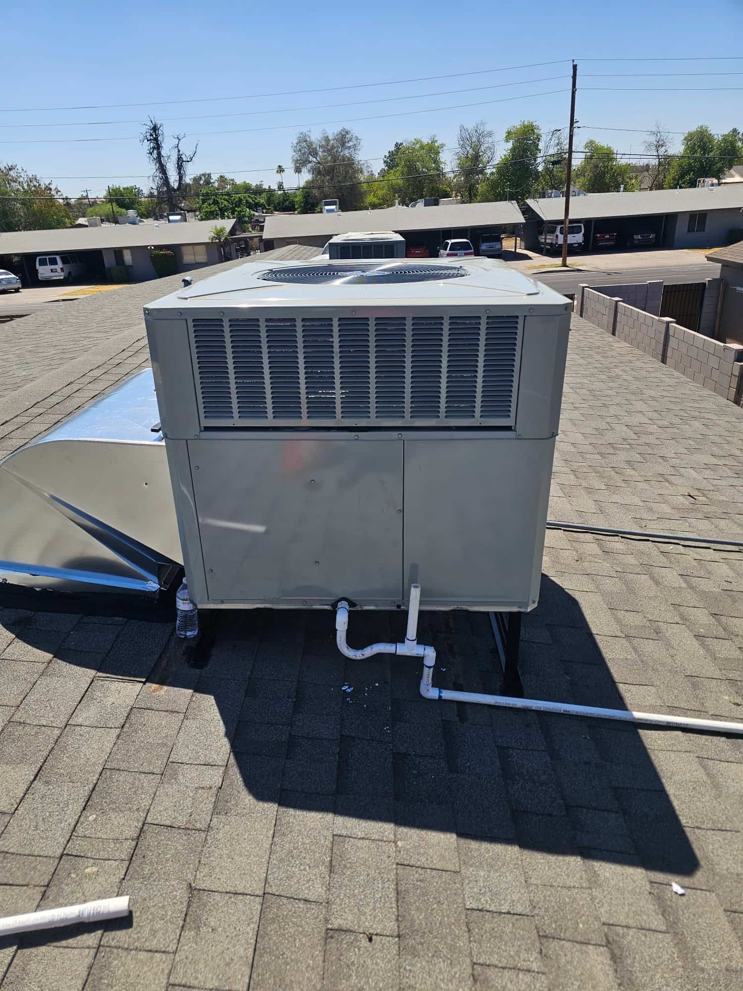 New rooftop packaged HVAC unit set on curb with connected condensate drain piping and sealed roof penetration.