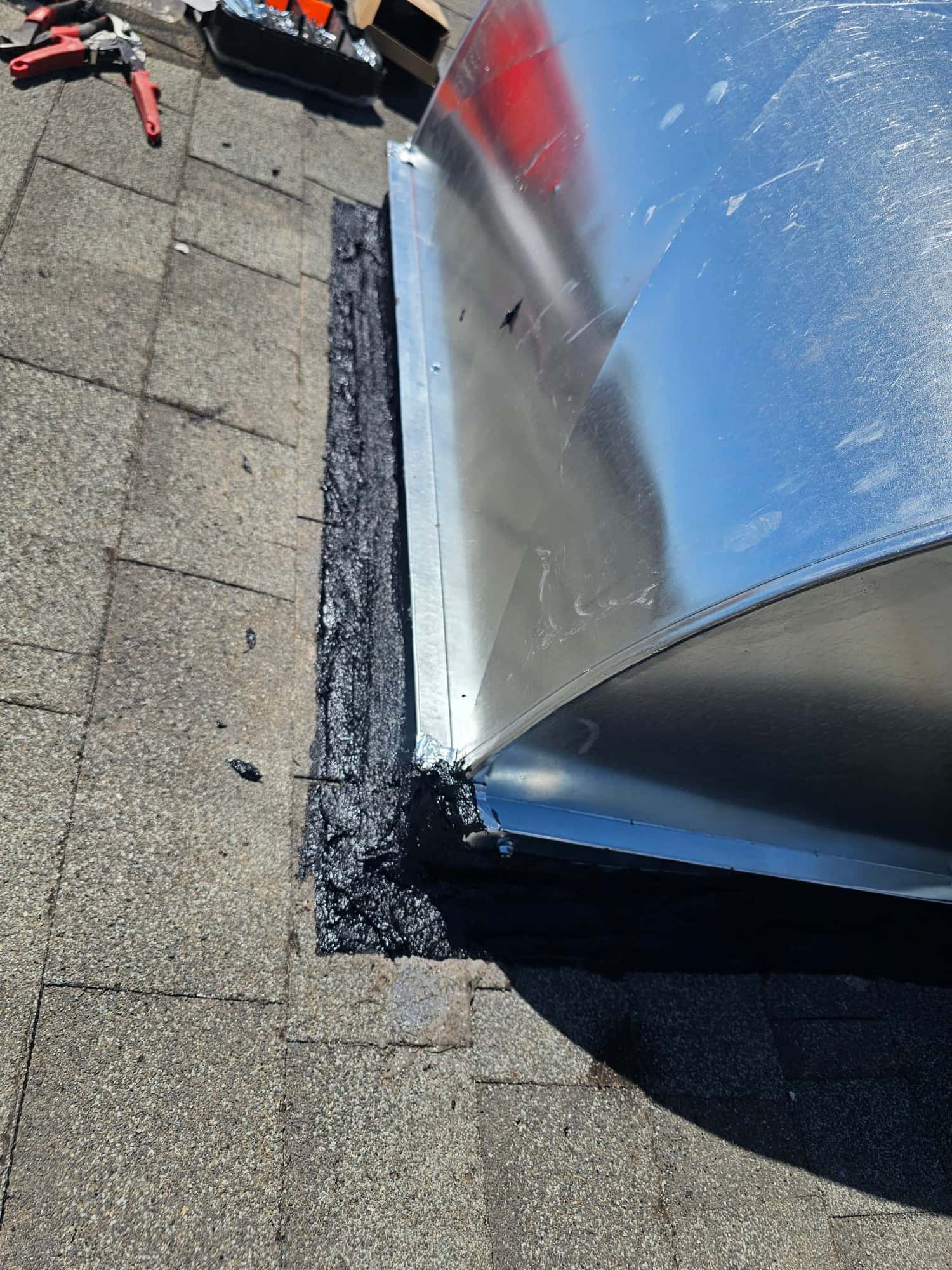 Roof curb or duct penetration is sealed with roofing mastic around the metal flashing on asphalt shingles.