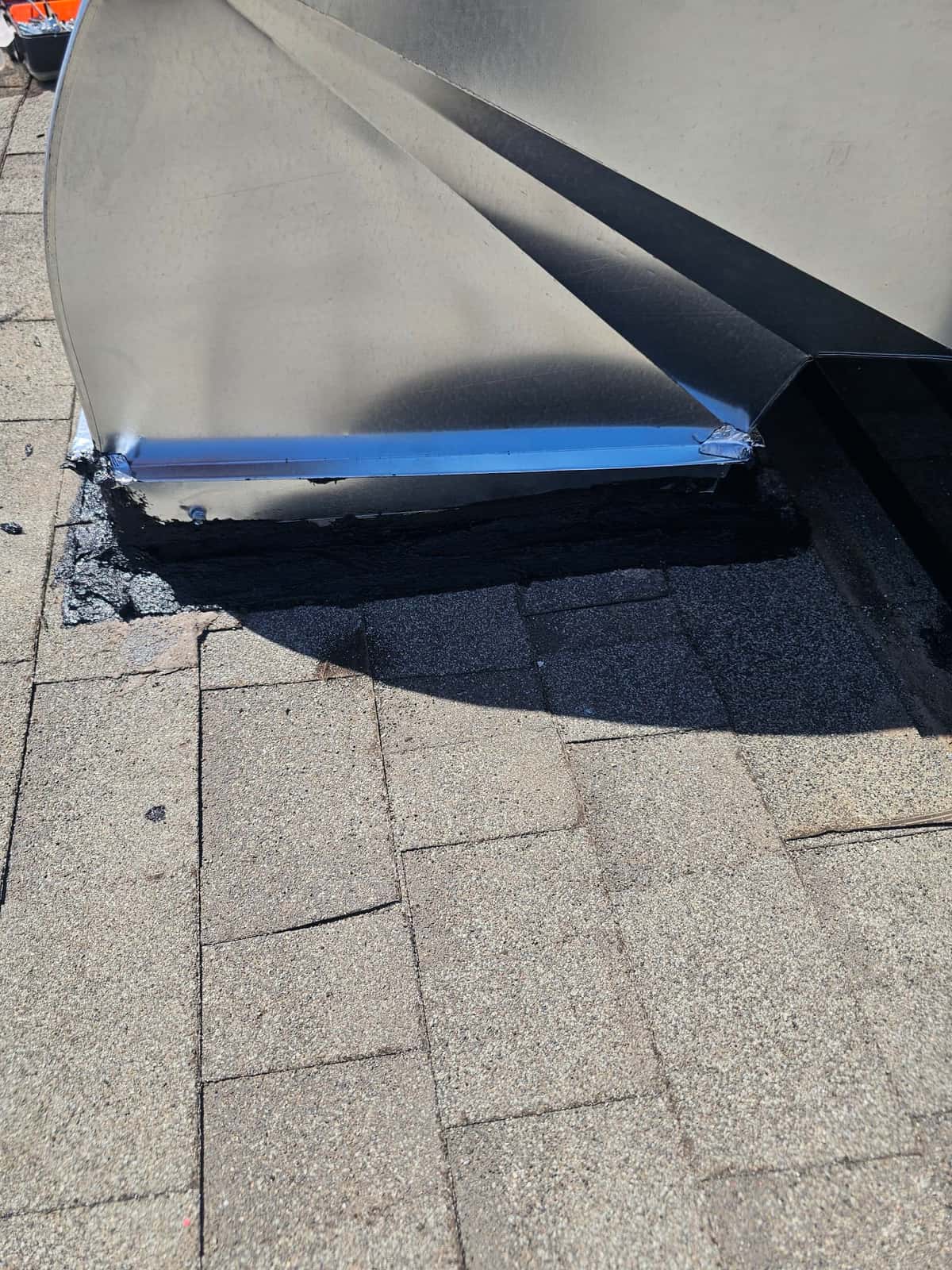 Sheet-metal duct curb on a shingle roof with fresh flashing and sealant applied around the base.