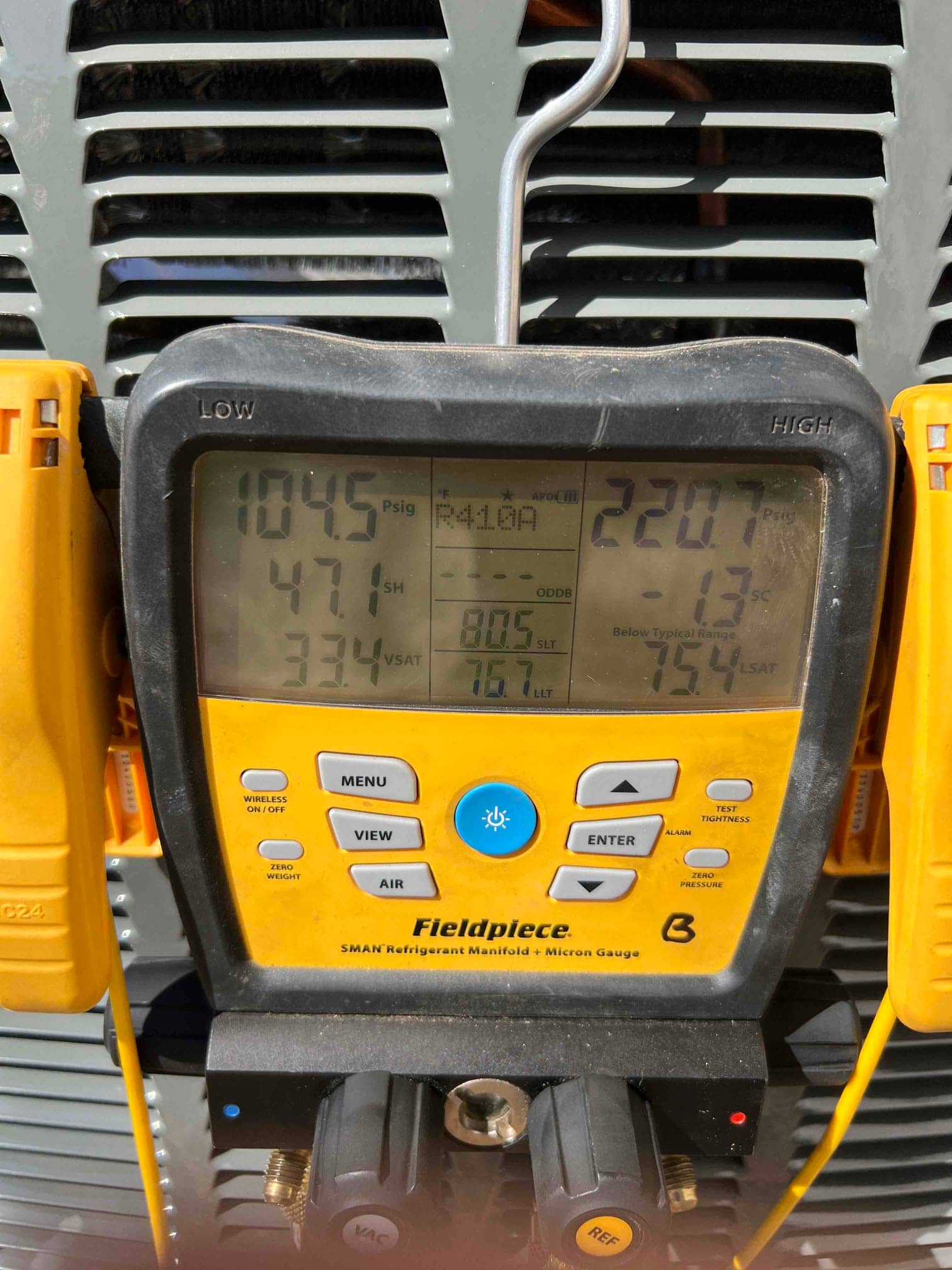 Digital manifold on the outdoor unit shows operating pressures and temperatures during system commissioning with refrigerant R-410A.