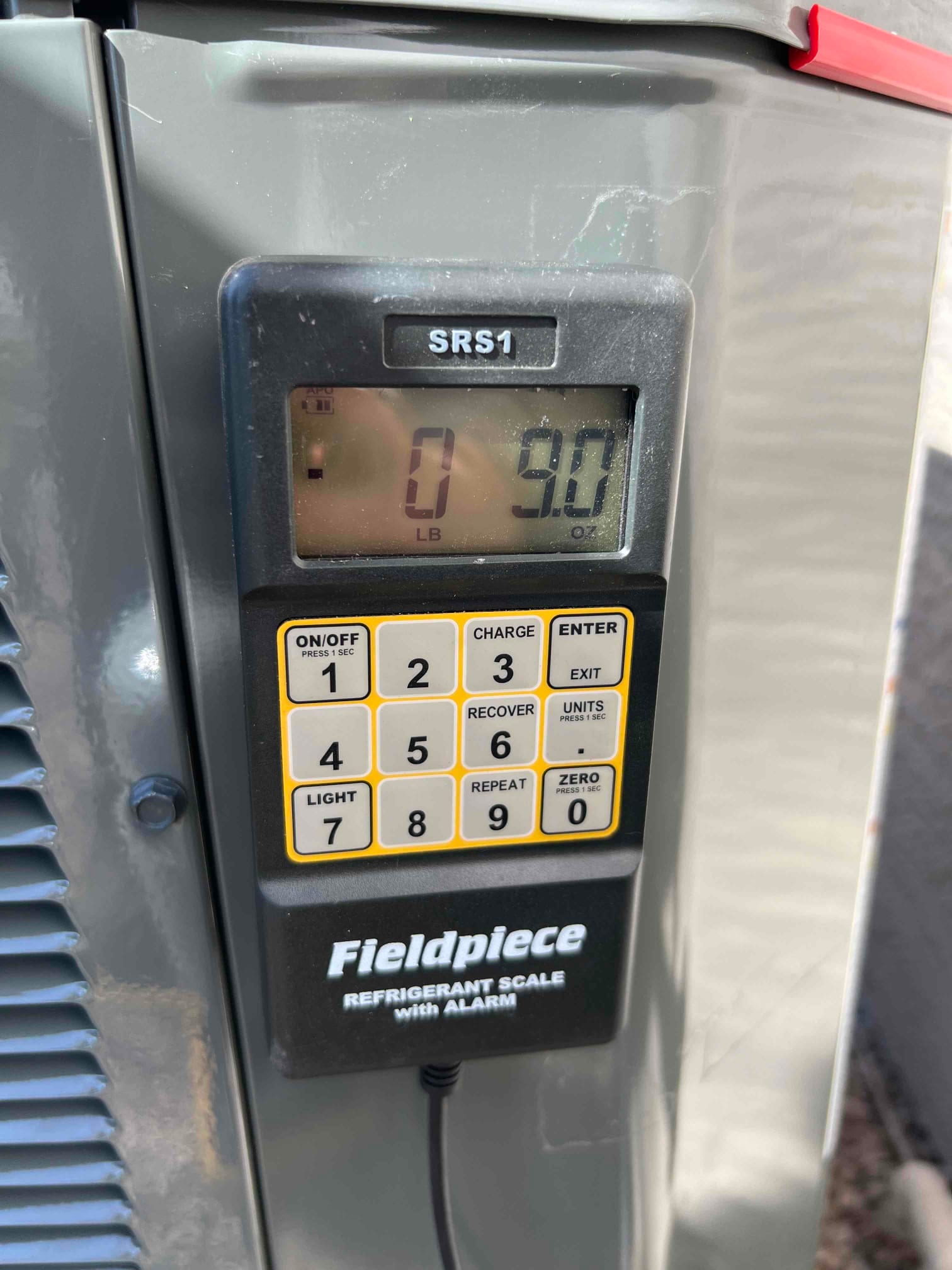 Digital refrigerant scale attached at the outdoor unit displays 0 pounds 9.0 ounces during charging operations.