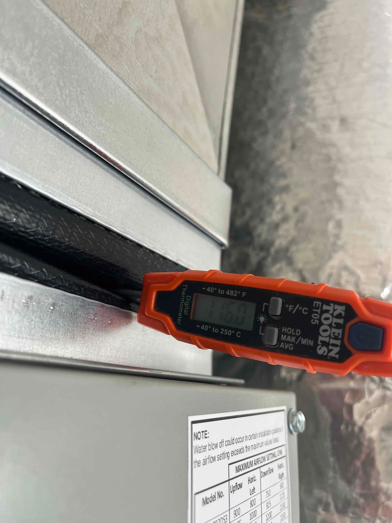 Digital thermometer inserted at the supply plenum reads 60°F, documenting cooled supply air temperature during commissioning.