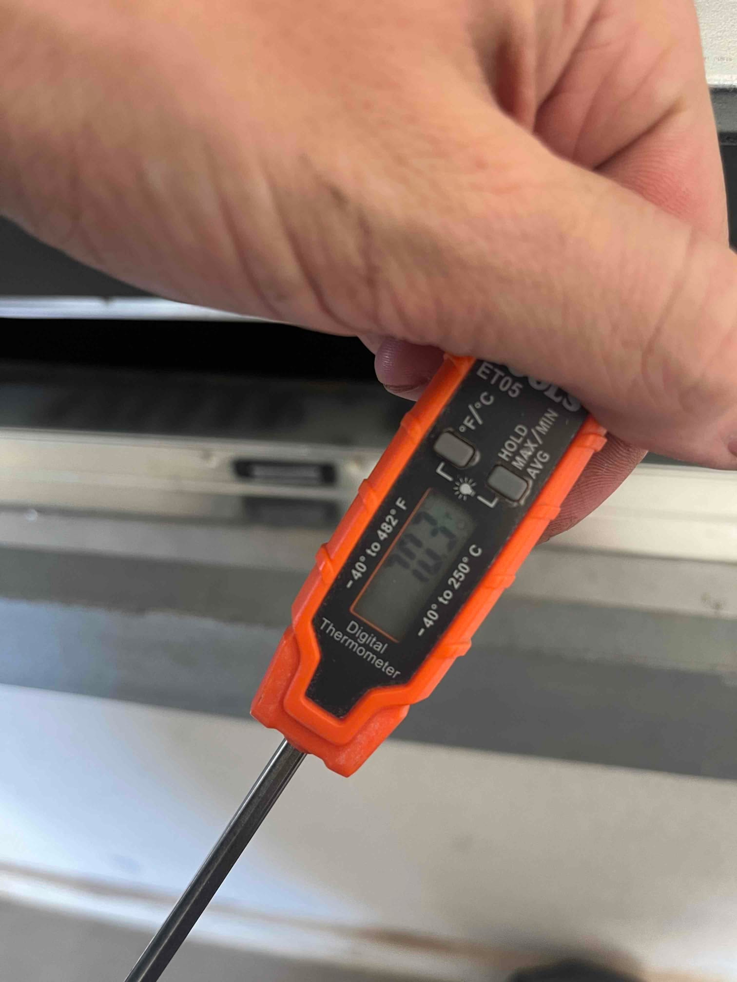 Digital thermometer probe measures return air at 70.3 degrees Fahrenheit during HVAC startup testing.