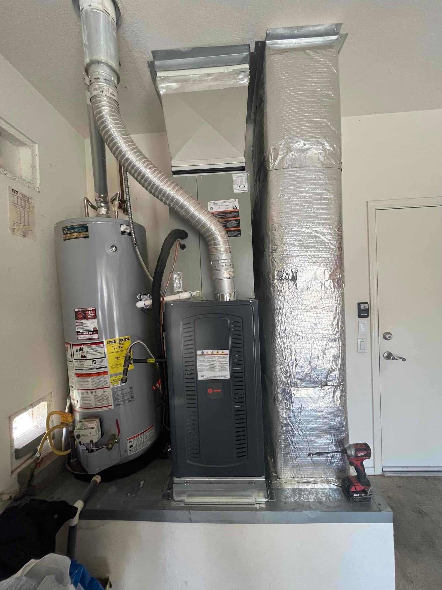 New gas furnace and evaporator cabinet installed on a platform with sealed duct transitions next to a water heater in the garage.