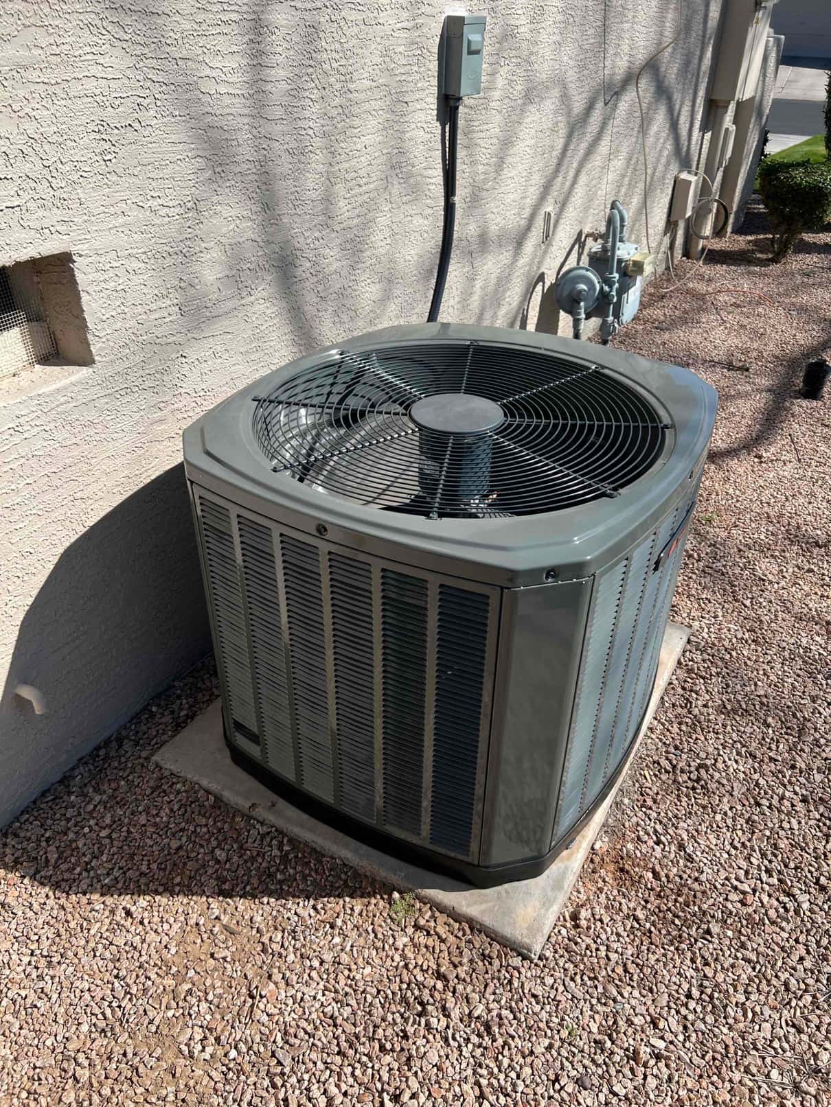 Outdoor condenser set on a level pad with electrical disconnect mounted on the wall and refrigerant lines routed into the home.
