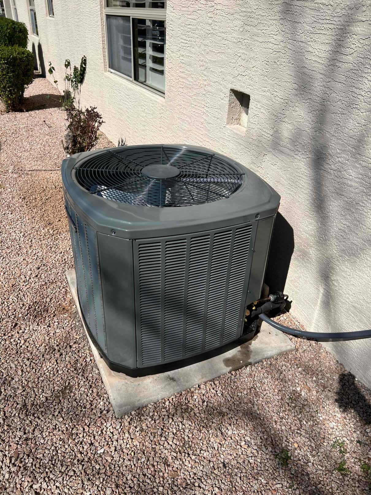 Outdoor condenser set on a level pad with insulated refrigerant line entering the wall at the installation site.