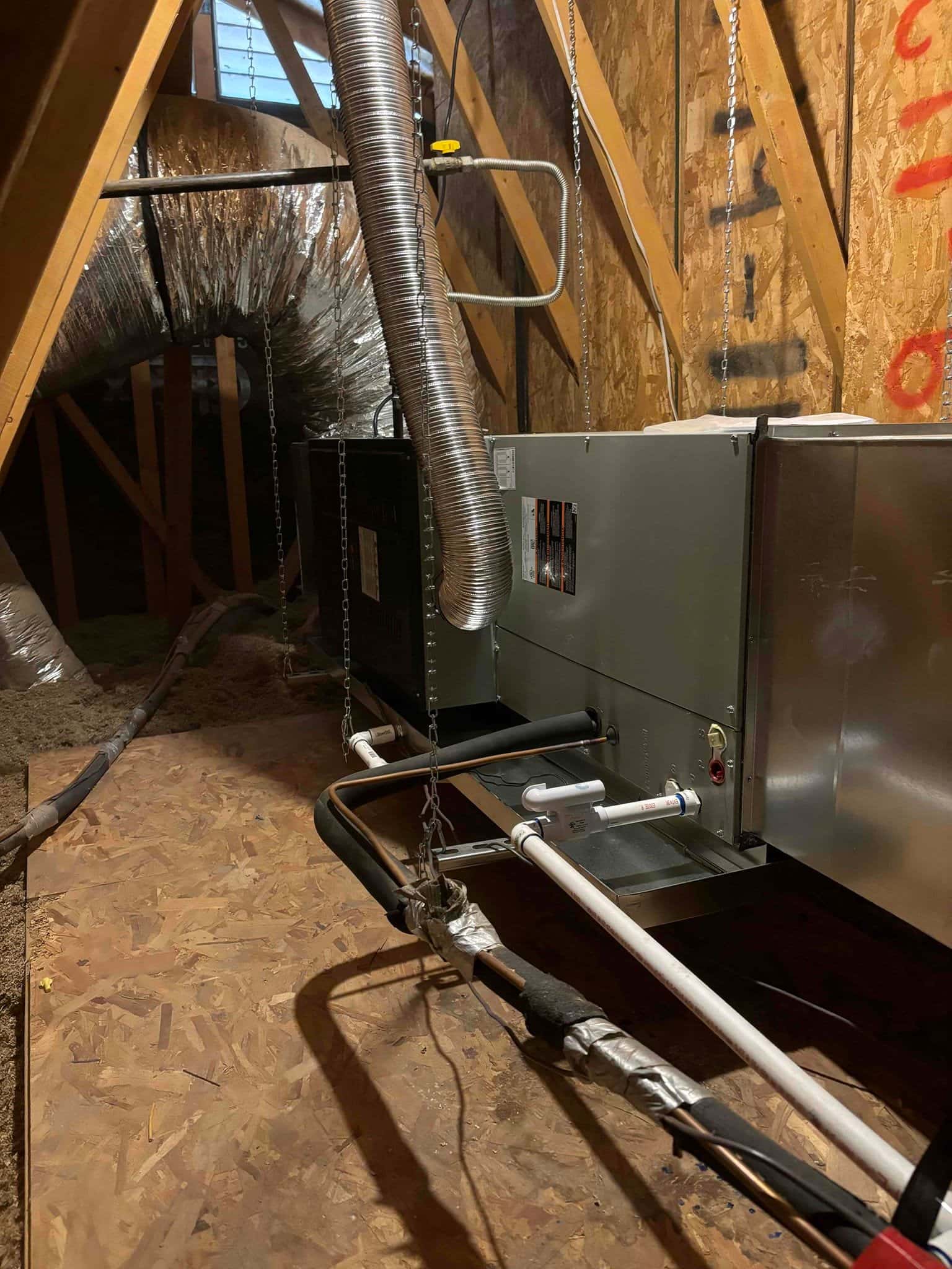 Air handler suspended in an attic with insulated refrigerant lines, condensate trap and drain, flex duct connections, and gas vent installed.