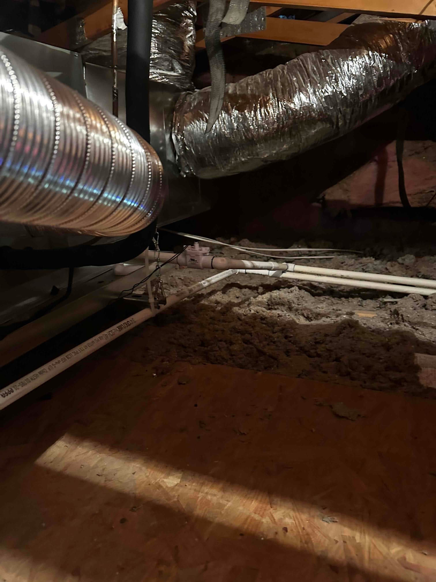Attic air handler with insulated flexible ducts, metal takeoff, and PVC condensate drain piping secured on a raised platform.