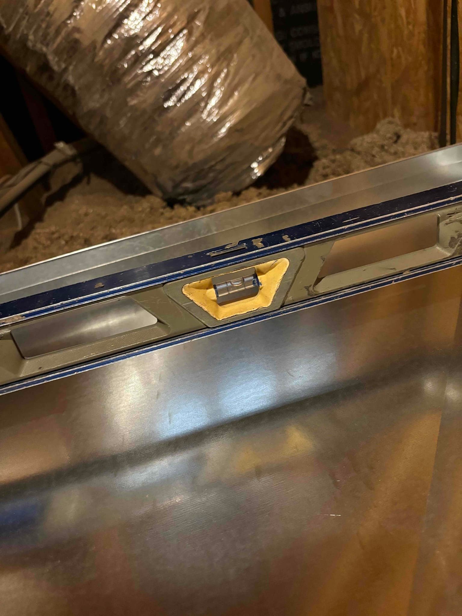 A bubble level placed on top of new sheet-metal ductwork in the attic to verify the section is installed level.