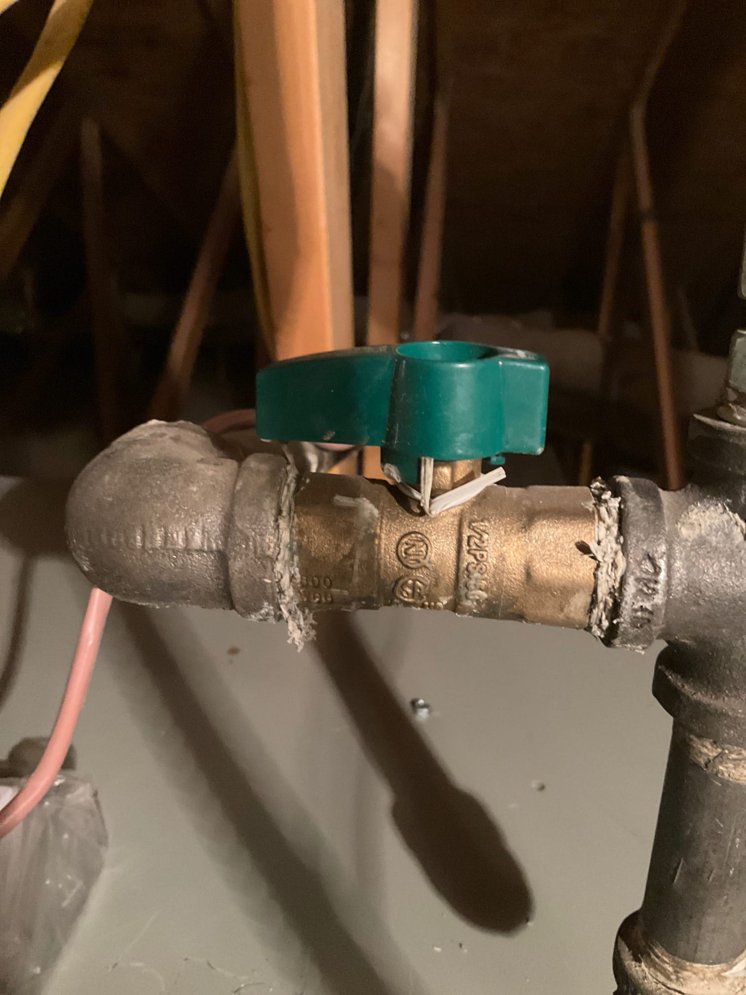 Close-up of a gas shutoff valve with green handle connected to black iron piping inside the attic installation area.