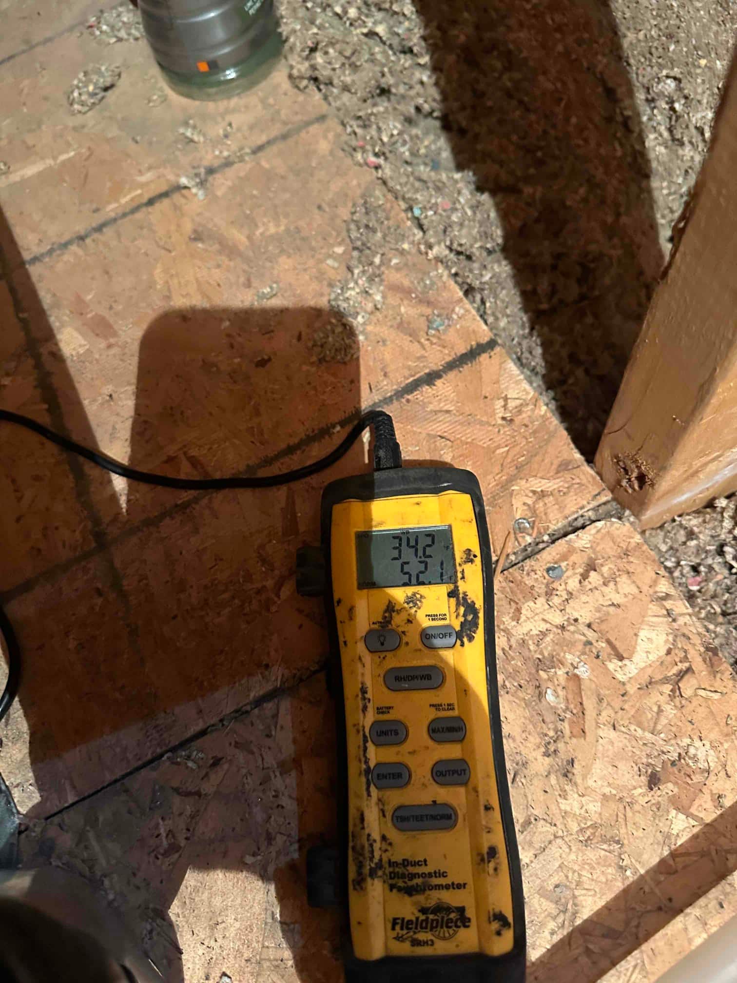 Digital in-duct thermometer displays 55.1 degrees Fahrenheit during supply air temperature check in the attic.