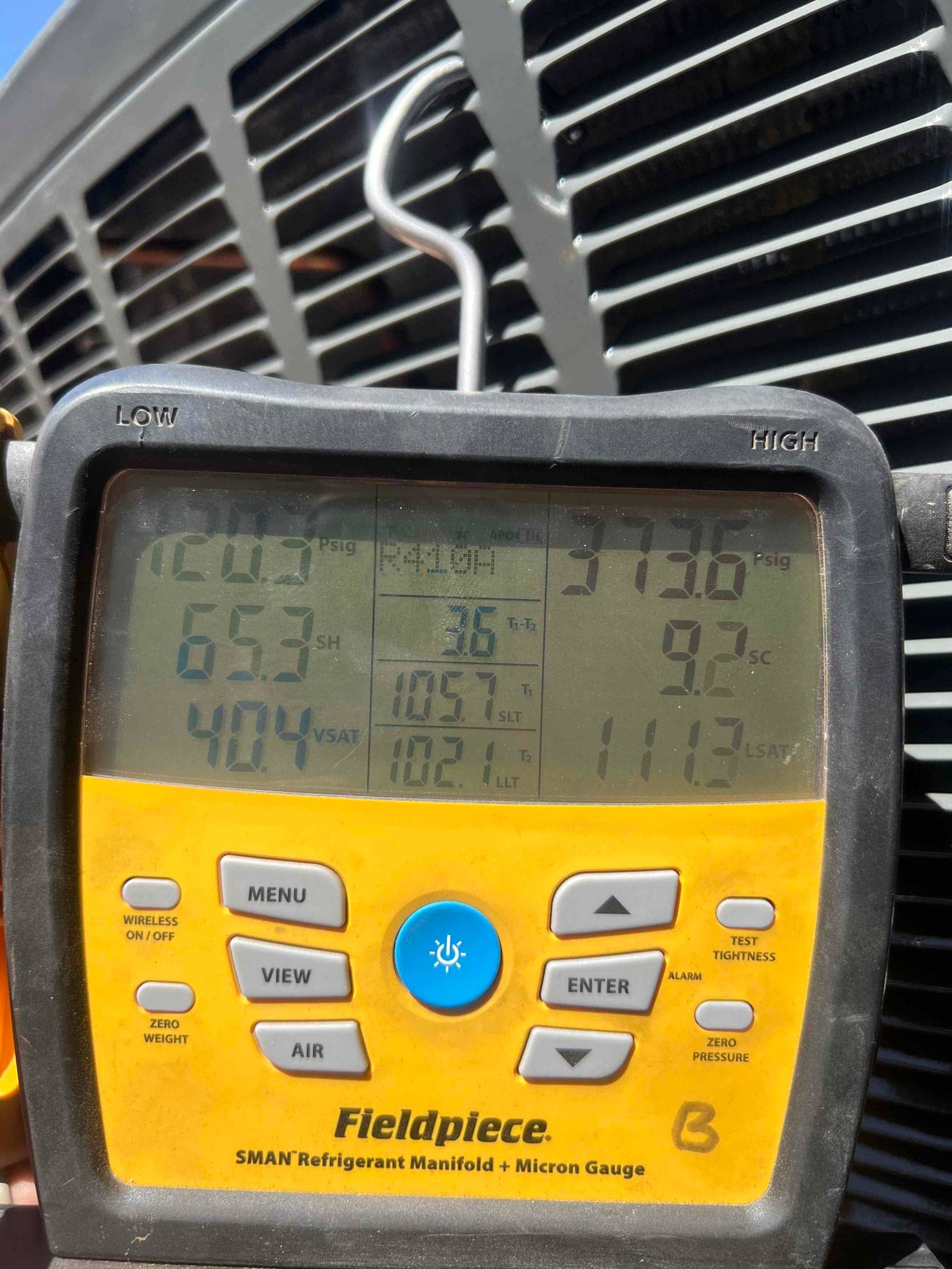 Digital manifold attached at the outdoor unit shows operating pressures with superheat and subcooling during system commissioning.