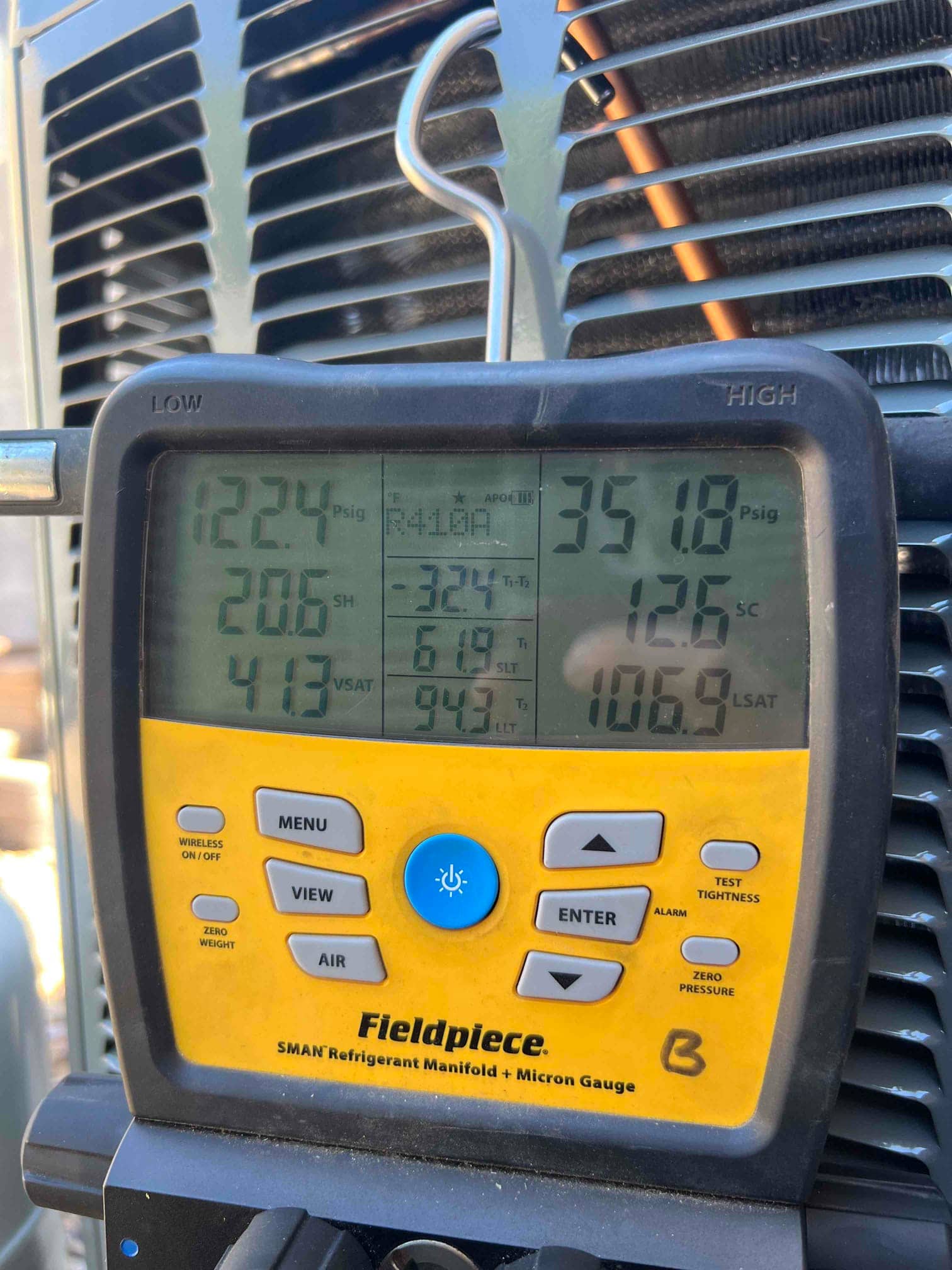 Digital manifold gauges on the outdoor unit show operating pressures while the air conditioning system runs after installation.