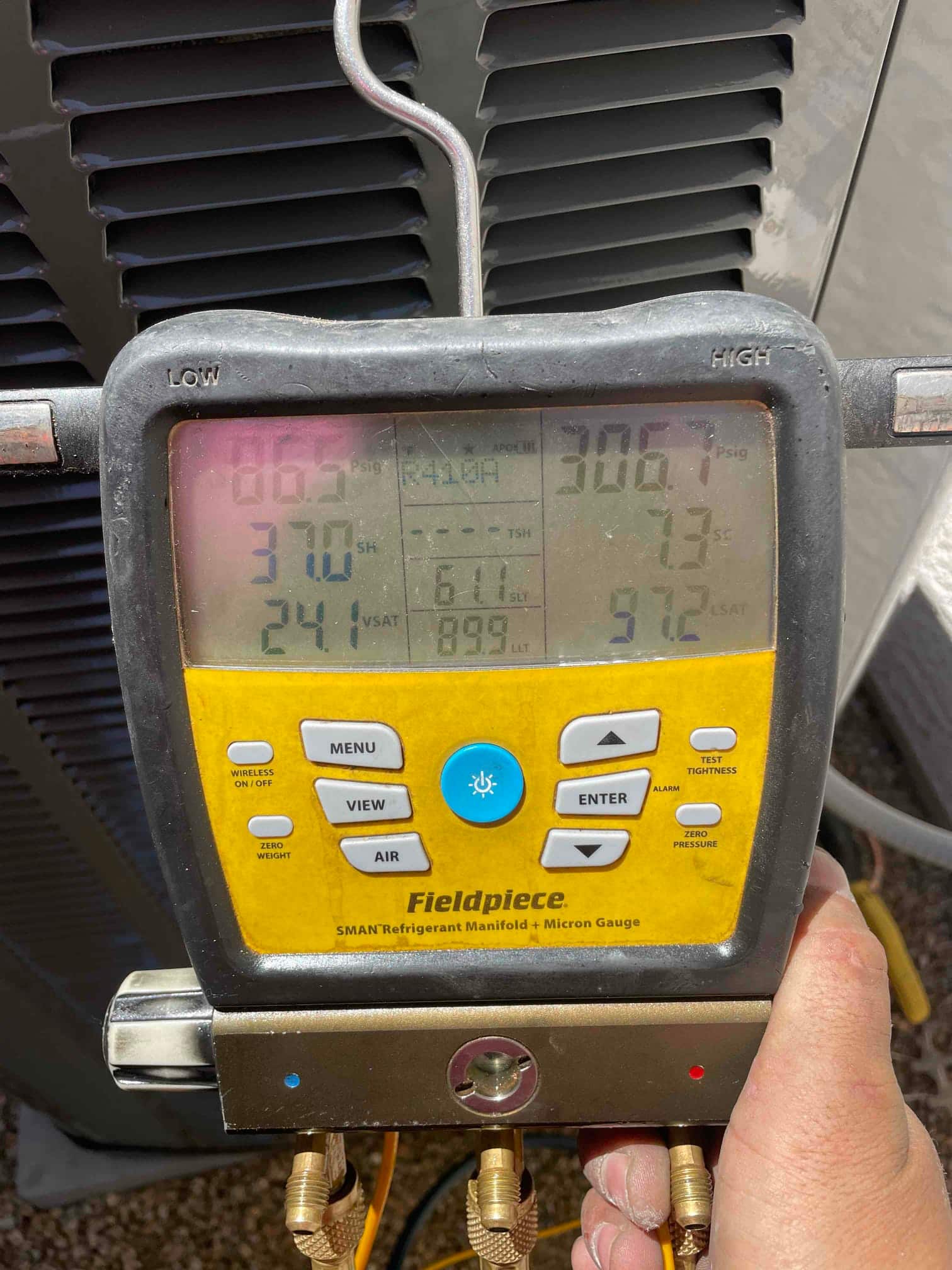 Digital manifold gauges on the outdoor unit show operating pressures with the system running during refrigerant commissioning.