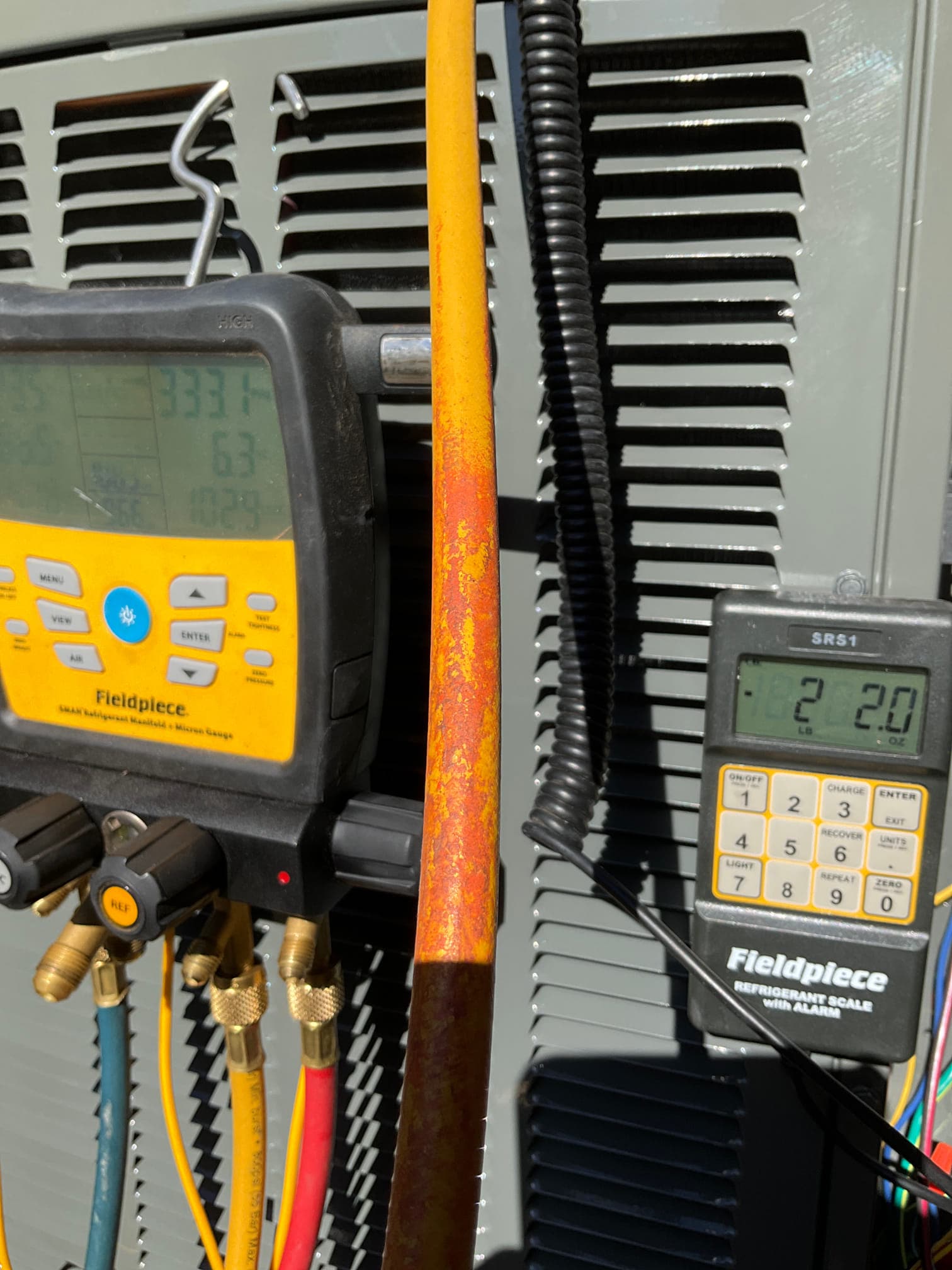 Digital manifold and refrigerant scale connected at the outdoor unit while recording operating pressures during system commissioning.