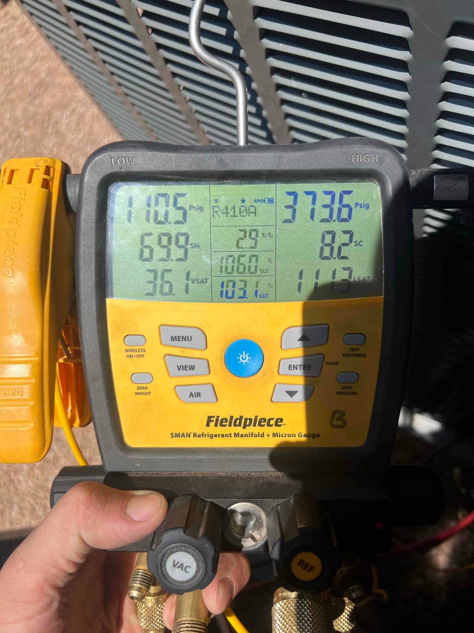 Digital manifold shows system operating pressures with refrigerant connected at the outdoor unit during commissioning.
