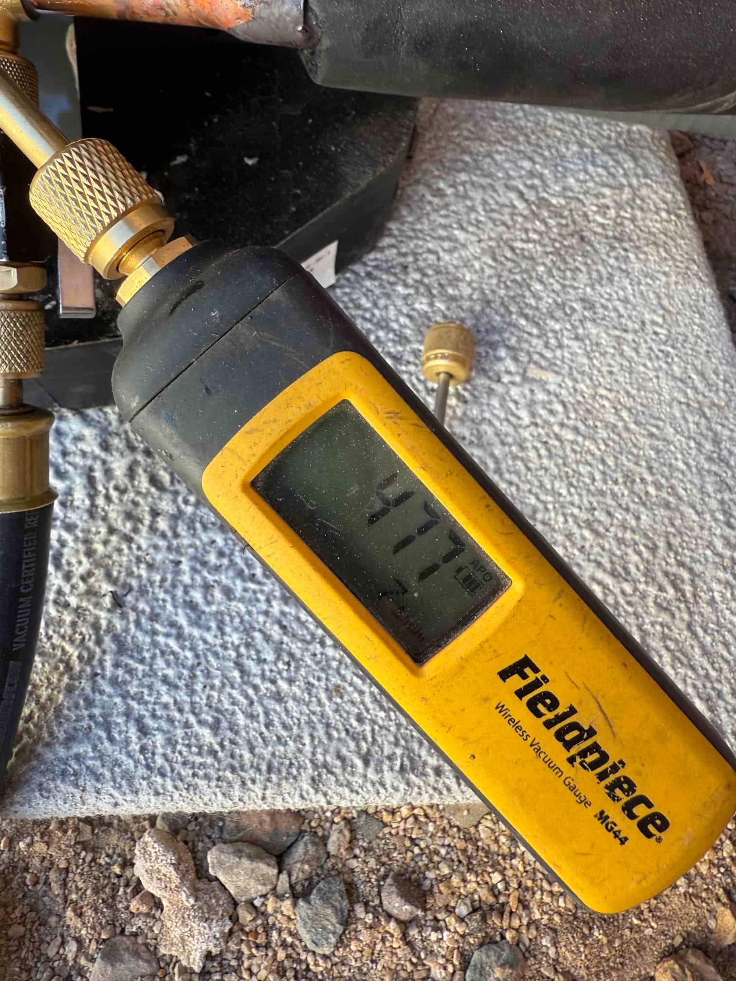 Digital micron gauge connected to the system shows 477 microns, confirming a deep vacuum during evacuation before refrigerant charging.