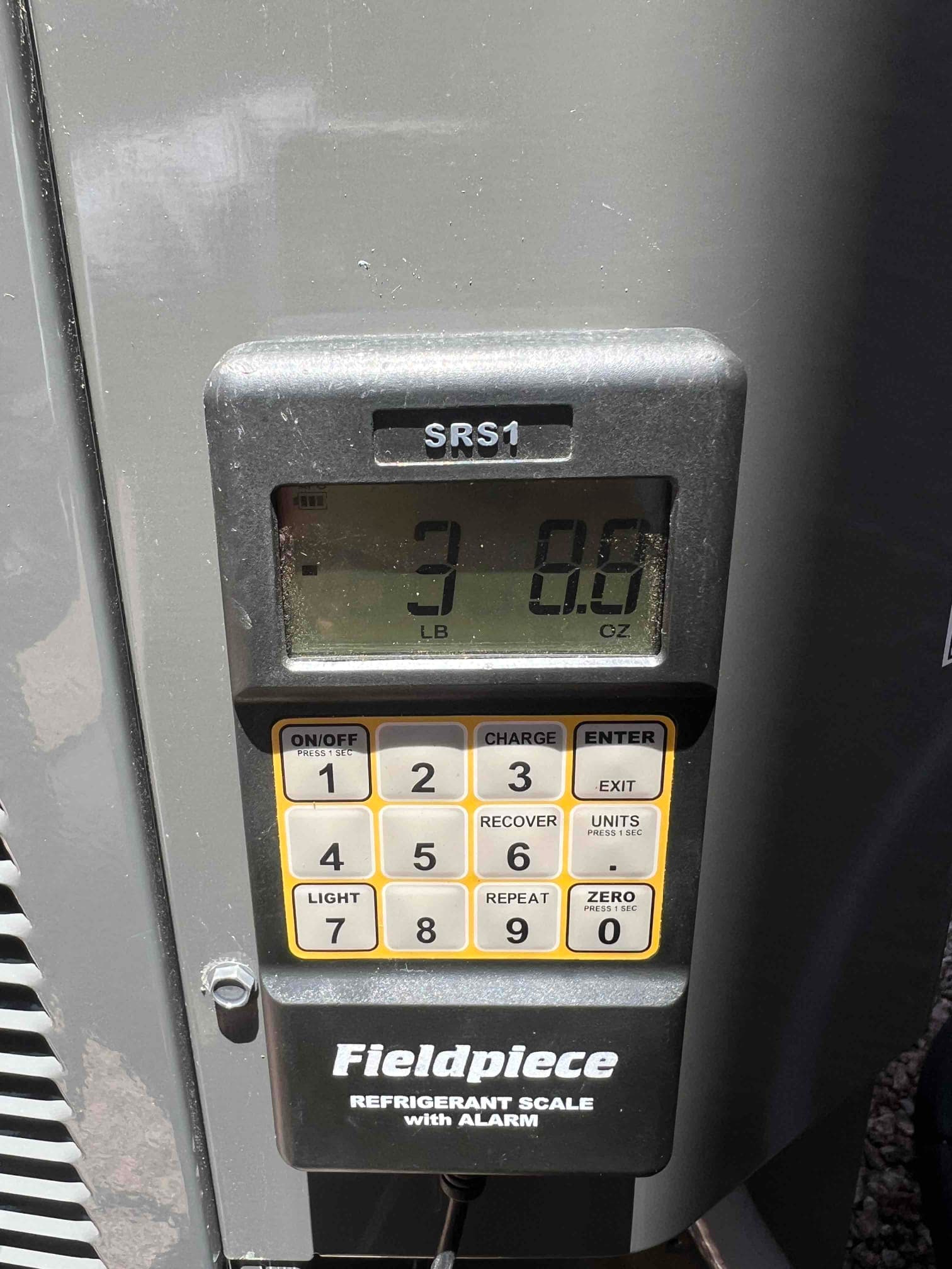 Digital refrigerant scale attached at the outdoor unit shows the charged refrigerant weight during system commissioning.