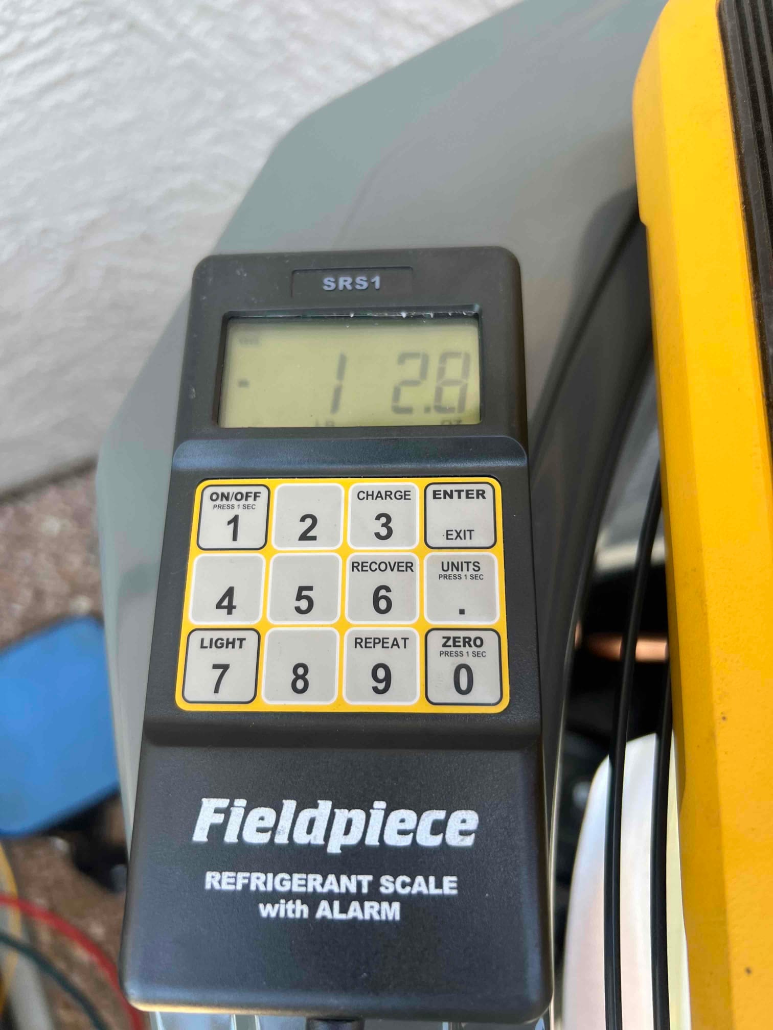 Digital refrigerant scale controller shows a reading of 12.8 on the display during charging work at the condenser.