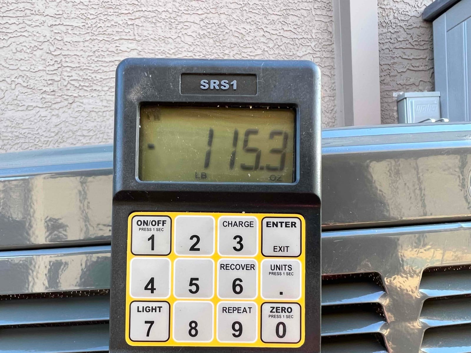 Digital refrigerant scale displays 115.3, documenting charge weight during installation beside the outdoor condenser unit.