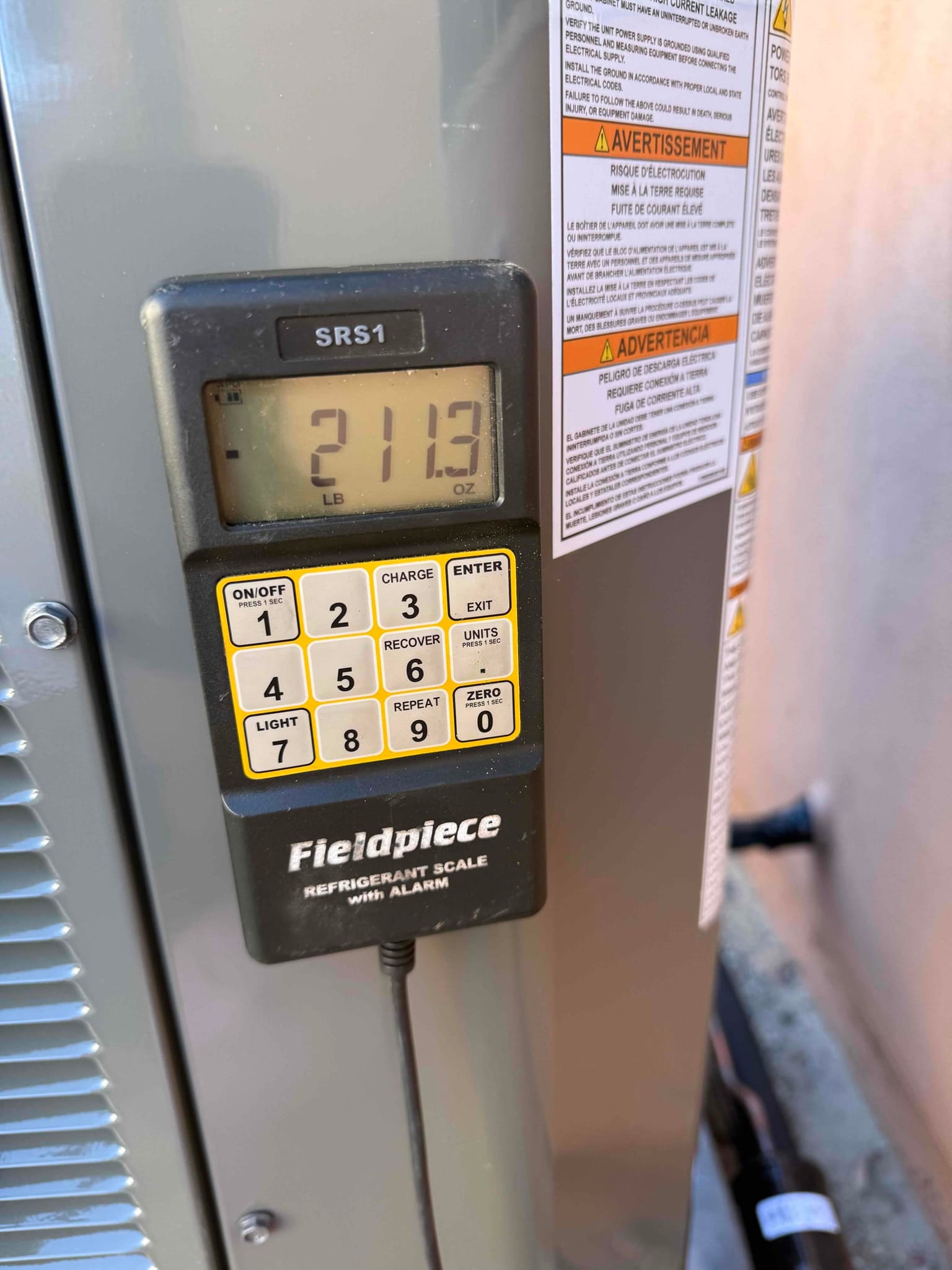Digital refrigerant scale displays 21.13 pounds during charging work beside the outdoor condenser cabinet.