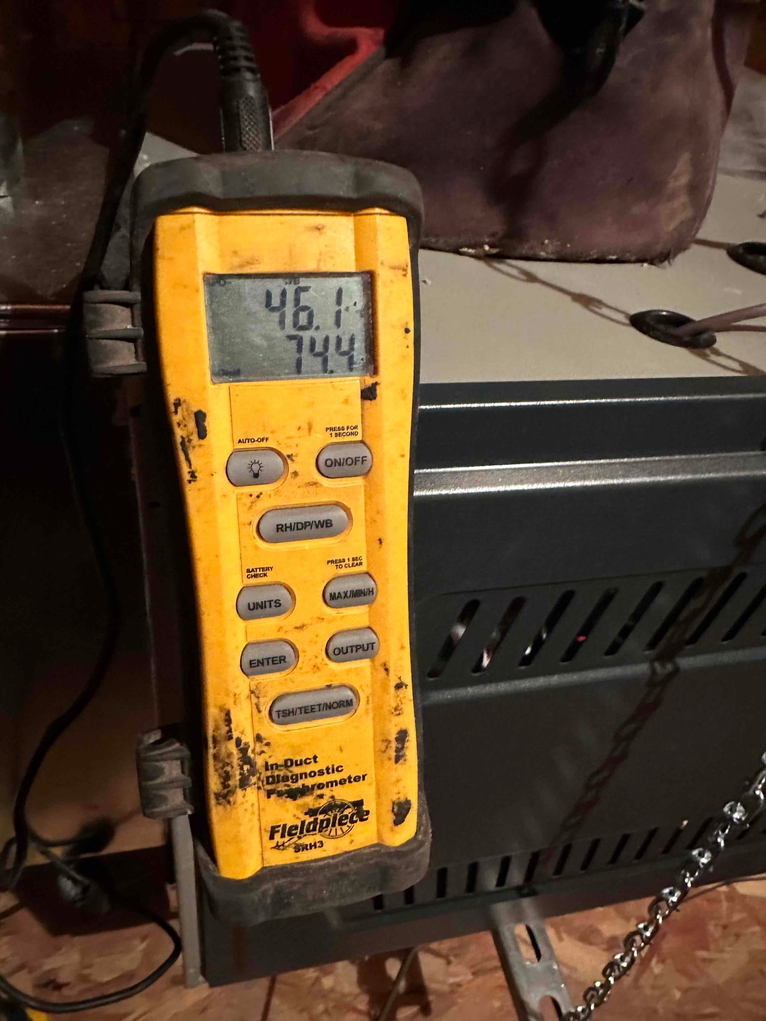 Digital thermometer displays 46.1°F and 74.4°F while measuring air temperatures during HVAC commissioning near the indoor unit.