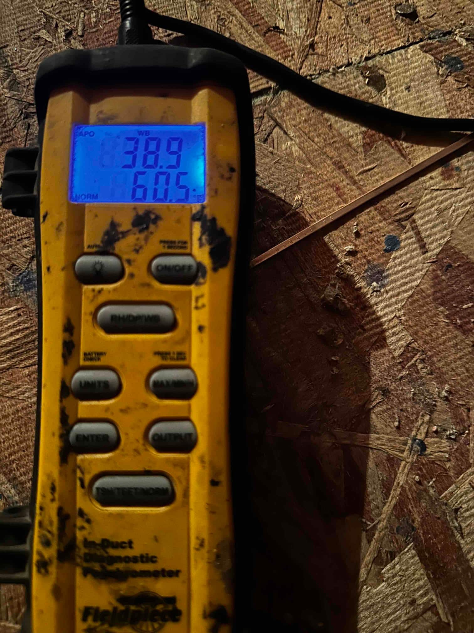 Digital thermometer displays 60.5 degrees Fahrenheit, documenting supply air temperature during cooling performance verification.