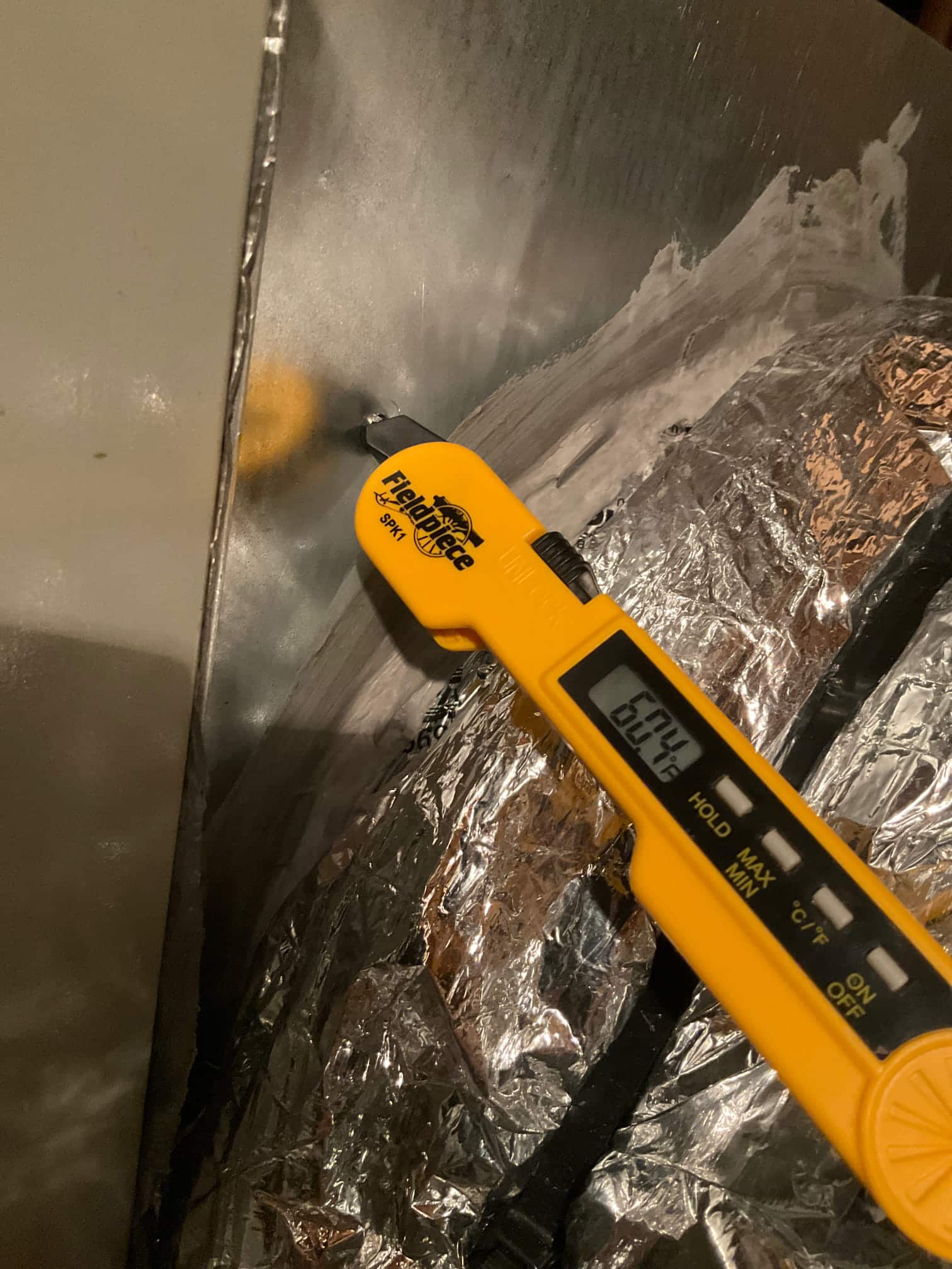 Digital thermometer probe inserted at duct measures 60.4 degrees Fahrenheit, documenting supply air temperature leaving the evaporator.