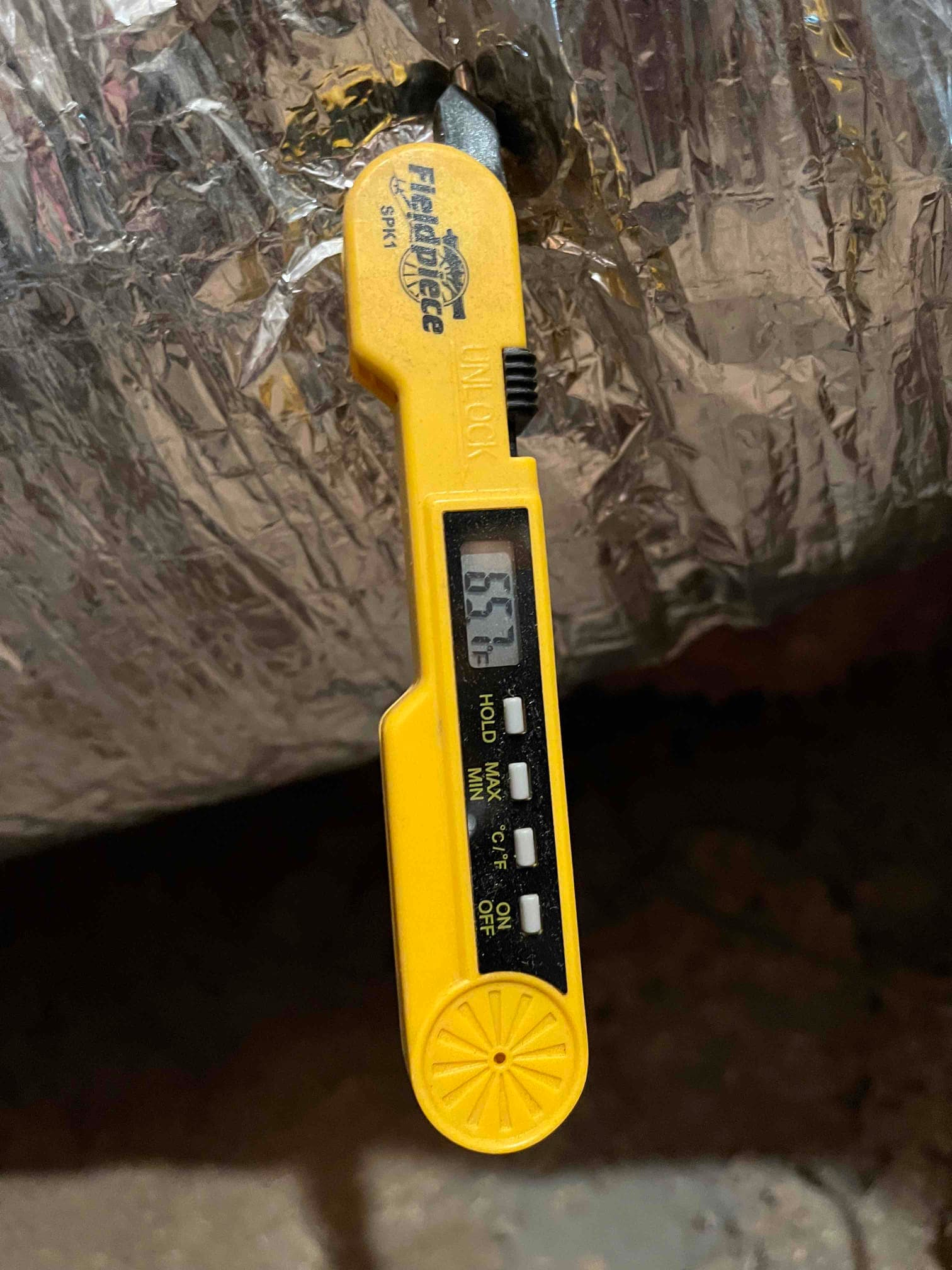 Digital thermometer probe inserted into insulated duct reads 65.7°F, documenting air-side temperature during system commissioning.