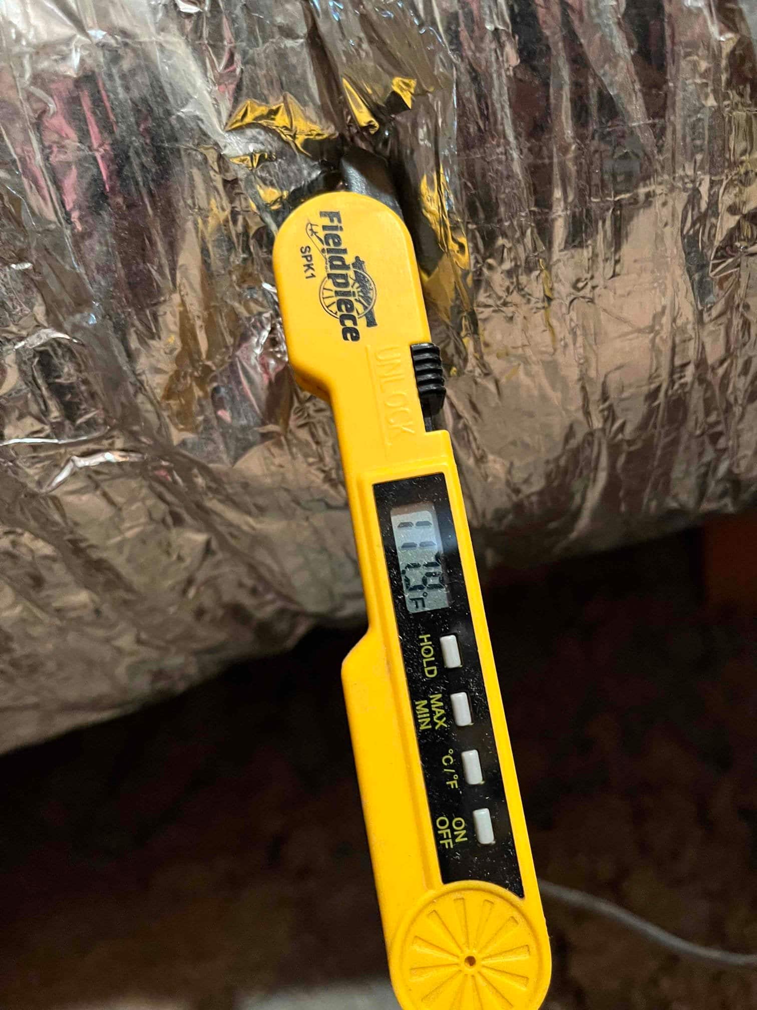Digital thermometer probe inserted into insulated duct shows 55.7°F, documenting supply air temperature after cooling.