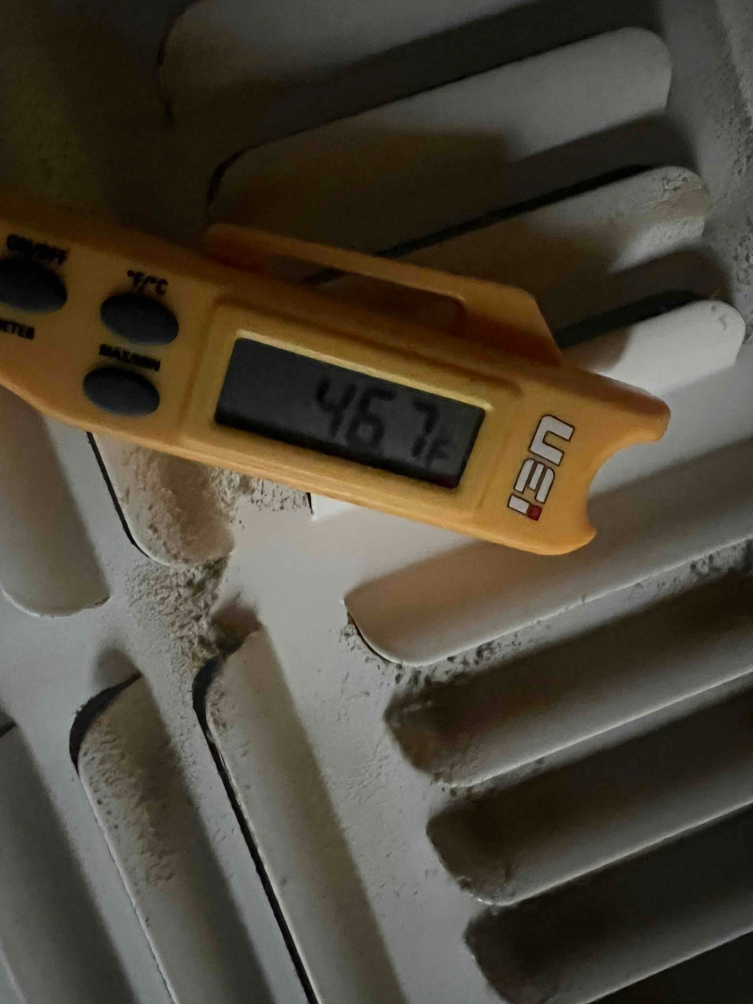Digital thermometer shows 46.7 °F on the vent grille surface during air conditioning operation.