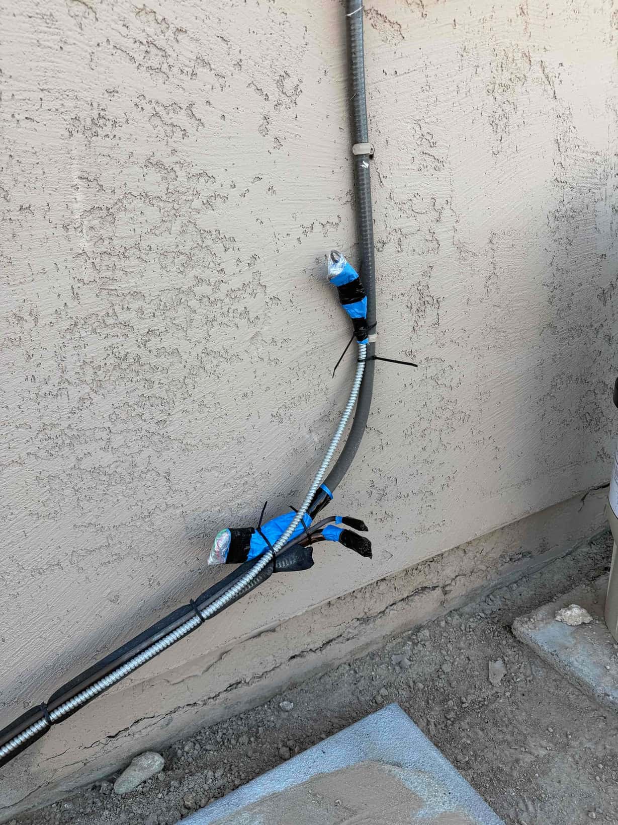 Flexible metal conduit and low-voltage cable are routed along the exterior wall, secured with straps and taped wire ends awaiting connection.