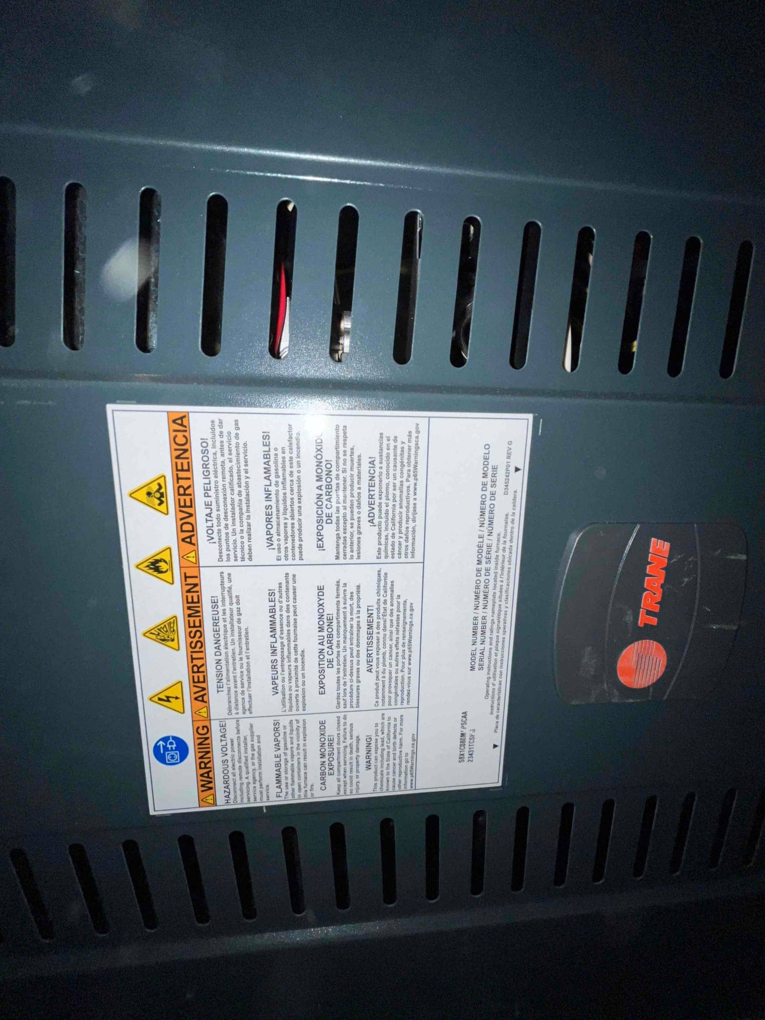 Furnace front panel with safety warning label and vent slots installed in place during HVAC system installation.