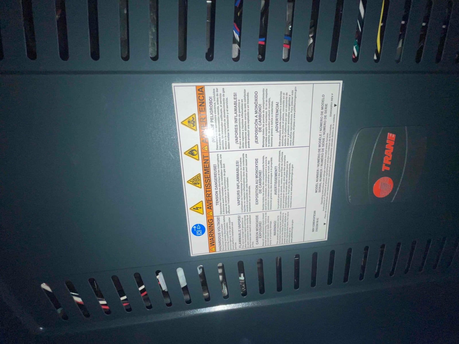 Gas furnace front panel with safety warning label installed, showing ventilation slots and internal wiring behind the cover.