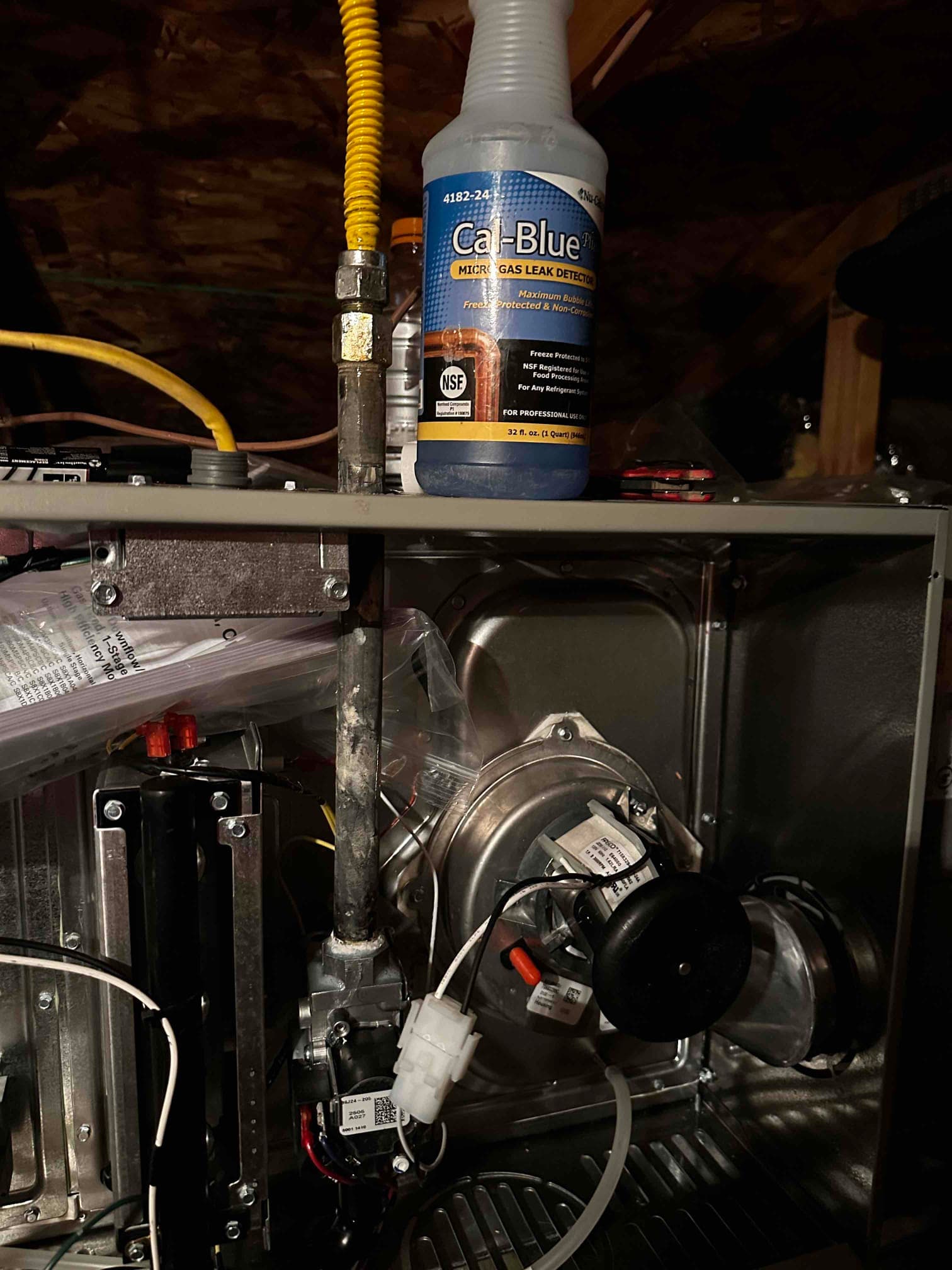 Gas furnace interior showing gas line connection, inducer assembly, wiring, and a gas leak detection solution bottle on the cabinet.